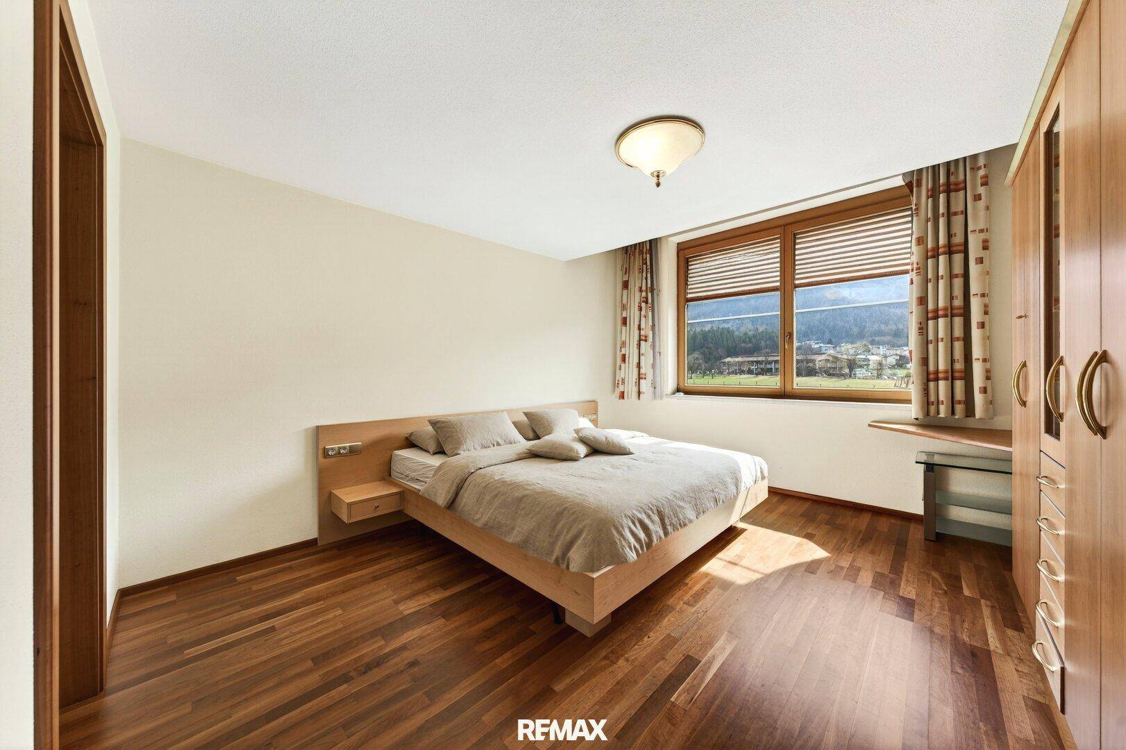 Schlafzimmer mit Doppelbett, Holzschrank und Holzboden mit Blick ins Grüne.