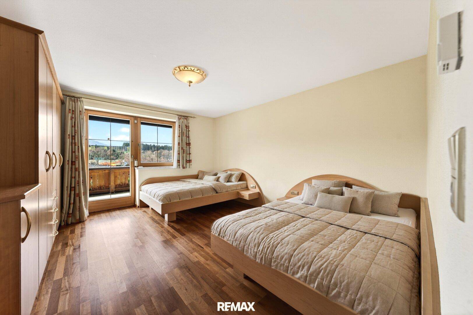 Schlafzimmer mit zwei Einzelbetten, Holzschrank und Zugang zum Balkon mit Aussicht.