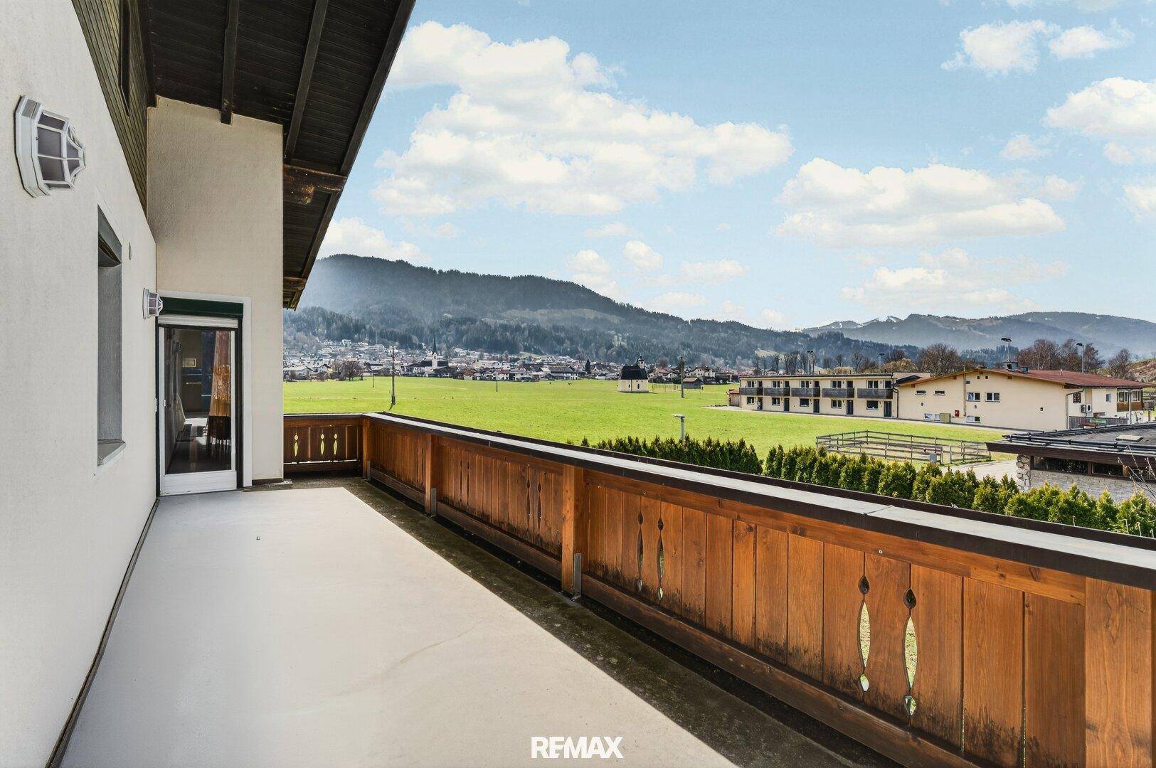 Großer Balkon mit Holzbalkonbrüstung und weitem Blick auf die Berge und grüne Landschaft.