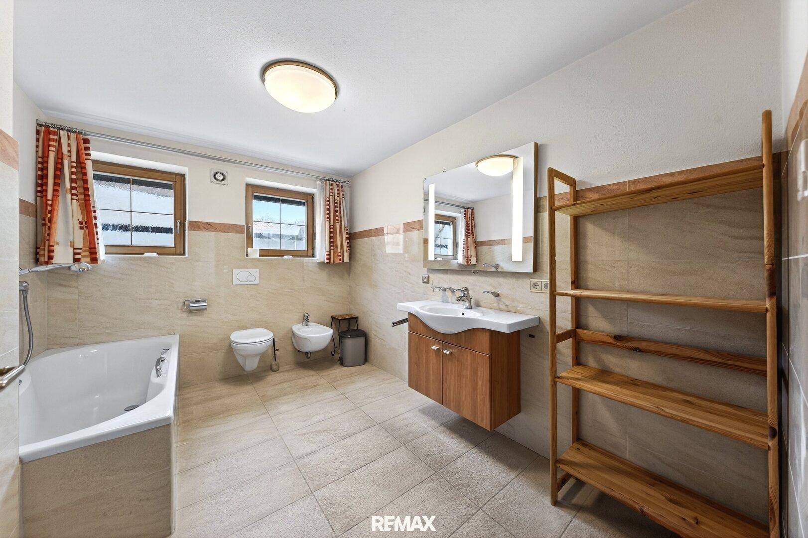 Helles Badezimmer mit Badewanne, Bidet und beigefarbenen Fliesen, mit Fenster für Tageslicht.