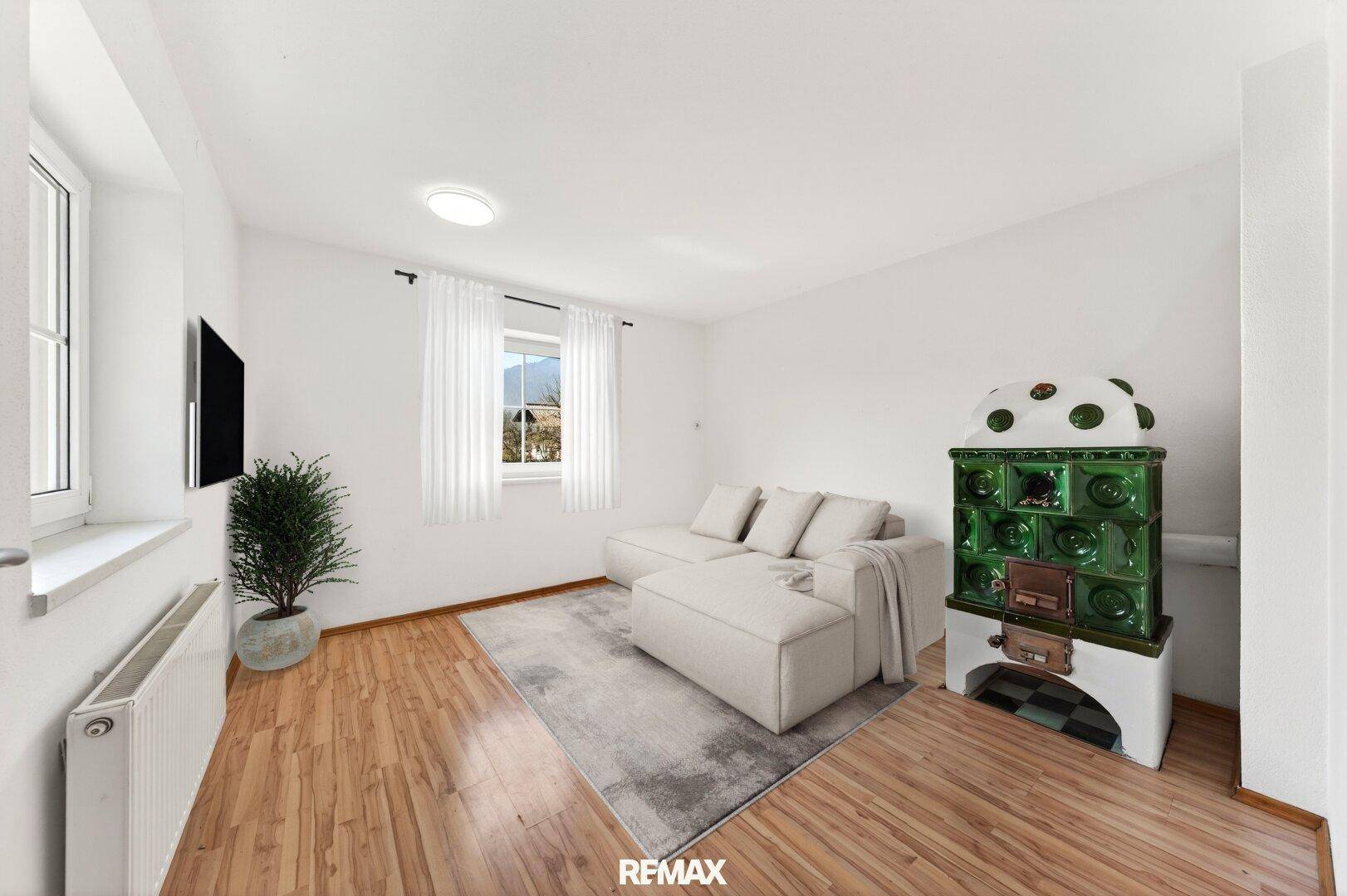 Helles Wohnzimmer mit Holzboden, modernem Sofa und traditionellem Kachelofen als Blickfang.