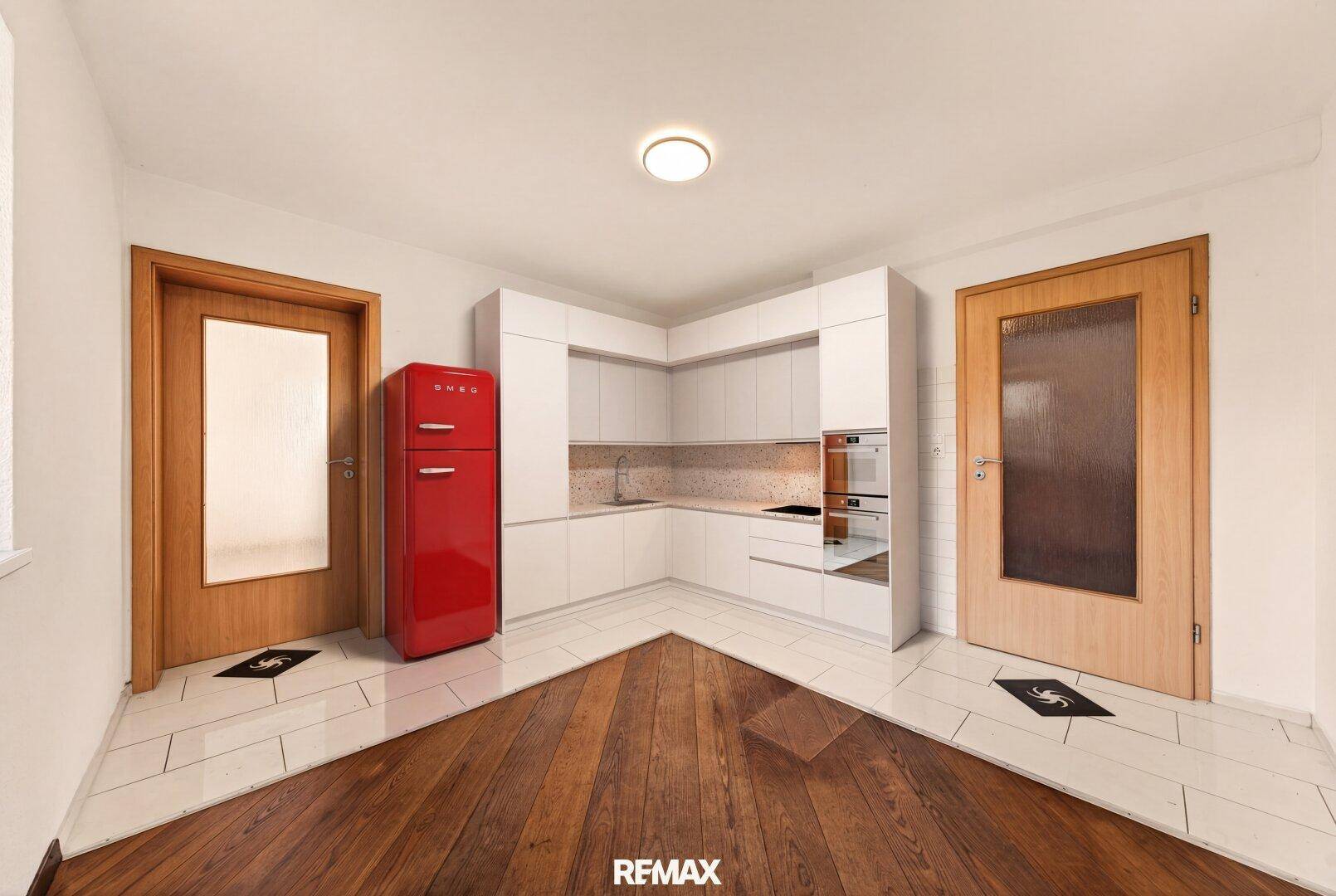 Moderne Küche mit weißen Schränken, integrierten Geräten und einem auffälligen roten Kühlschrank.