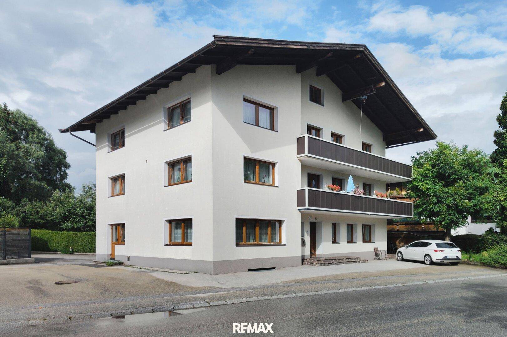 Mehrstöckiges Wohnhaus mit Balkonen und traditionellem Satteldach in ländlicher Umgebung.