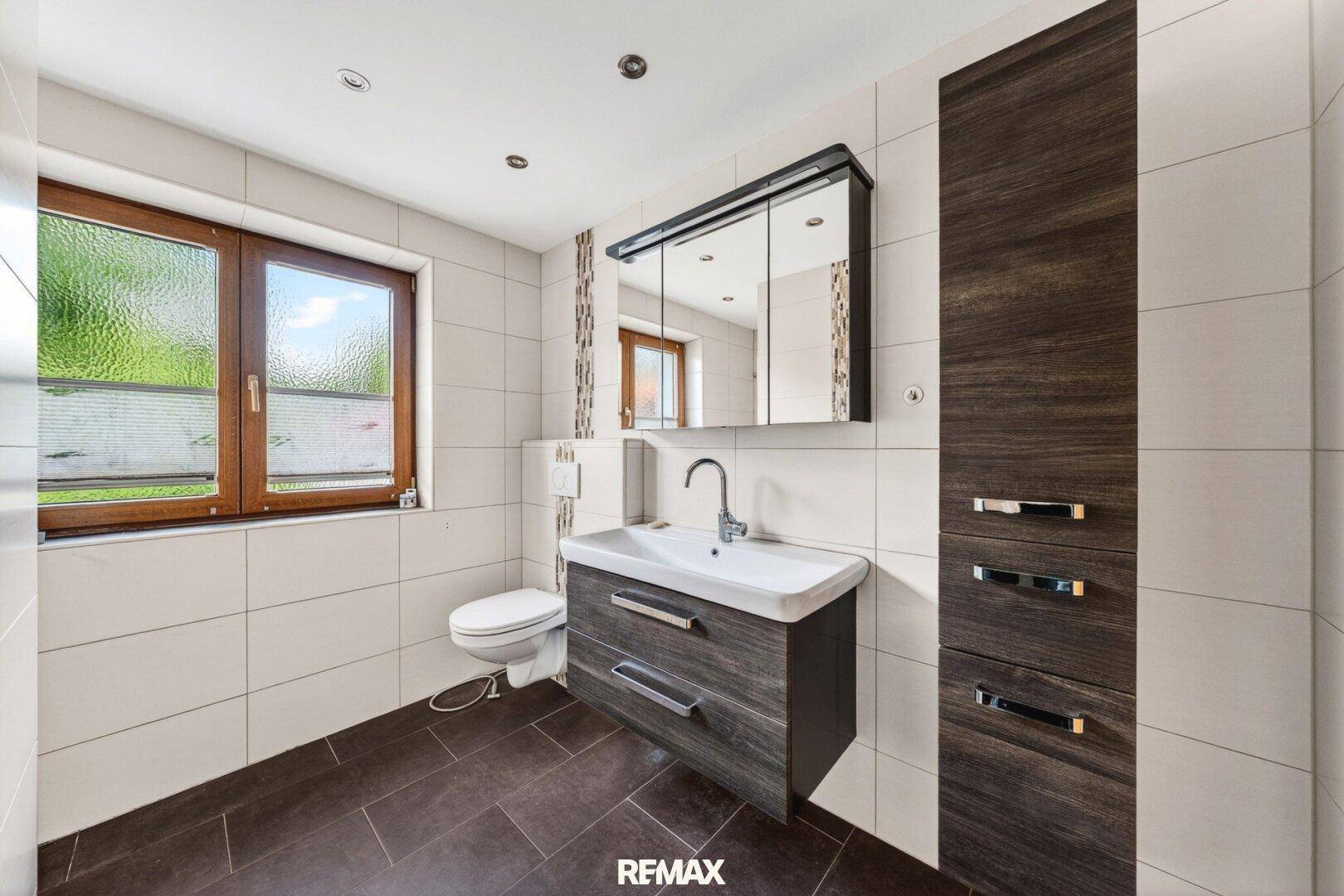 Modernes Badezimmer mit WC, Waschtisch, Spiegelschrank und Fenster.
