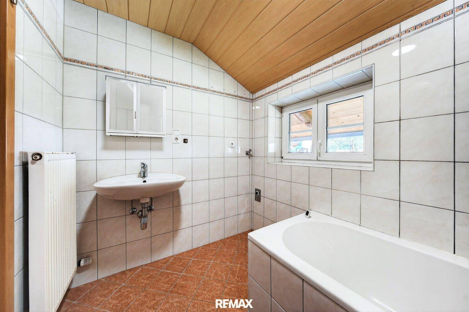 Gefliestes Badezimmer mit Badewanne, Waschbecken und Fenster für Tageslicht.