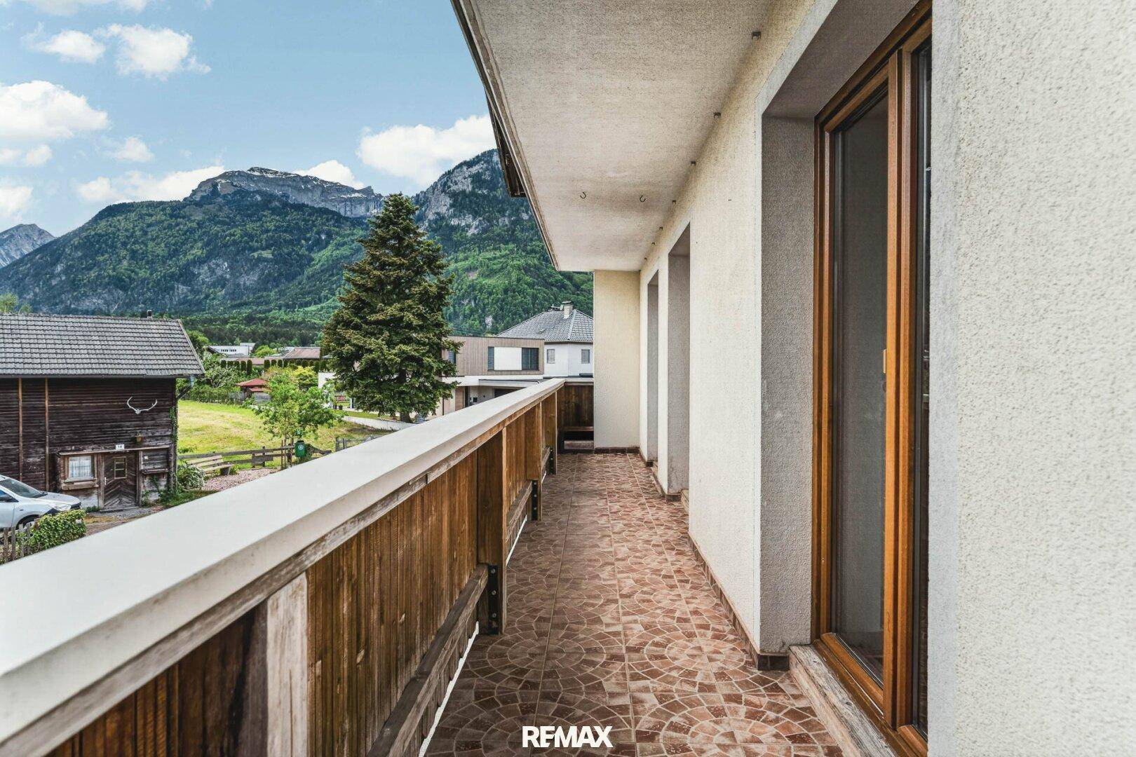 Langer Balkon mit Fliesenboden und Holzgeländer, der einen weiten Bergblick bietet.