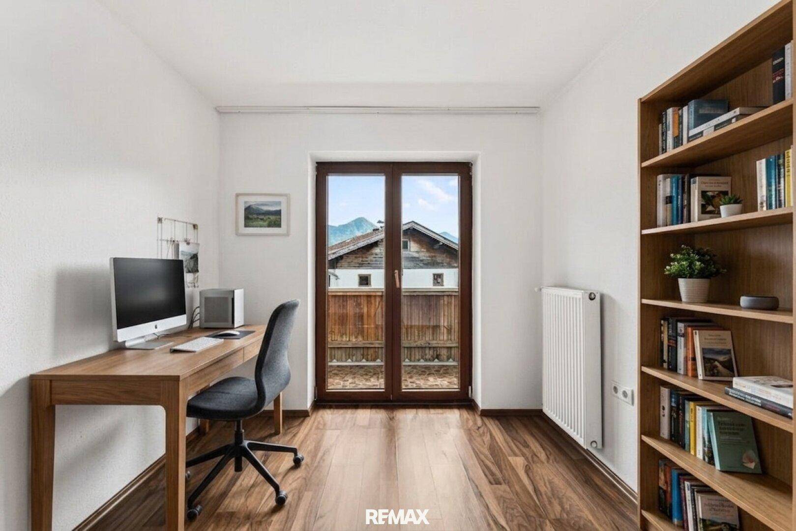 Helles Arbeitszimmer mit Schreibtisch, Bücherregal und Bergblick durch die Tür.