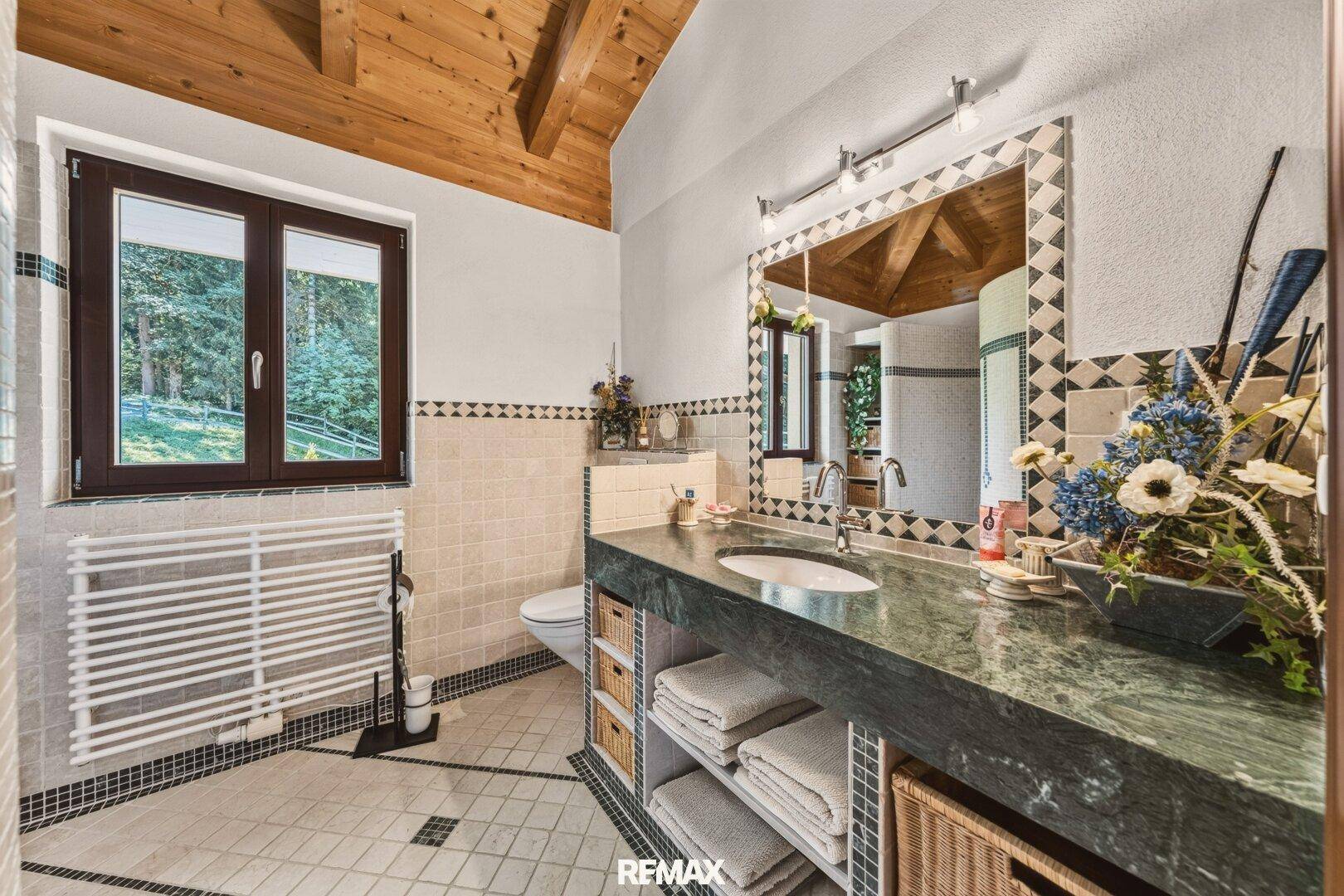 Badezimmer mit Doppelwaschbecken, grüner Marmorplatte und Holzbalkendecke.