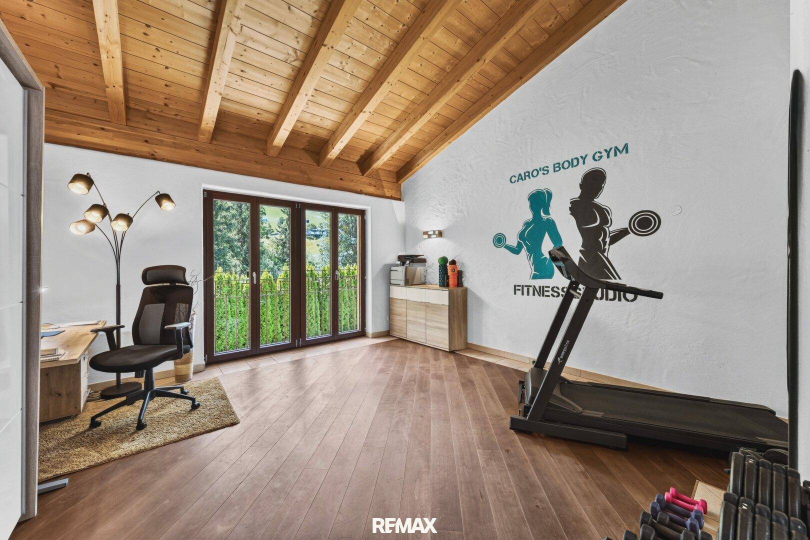 Fitnessraum mit Holzbalkendecke, Laufband und Zugang zum Außenbereich.