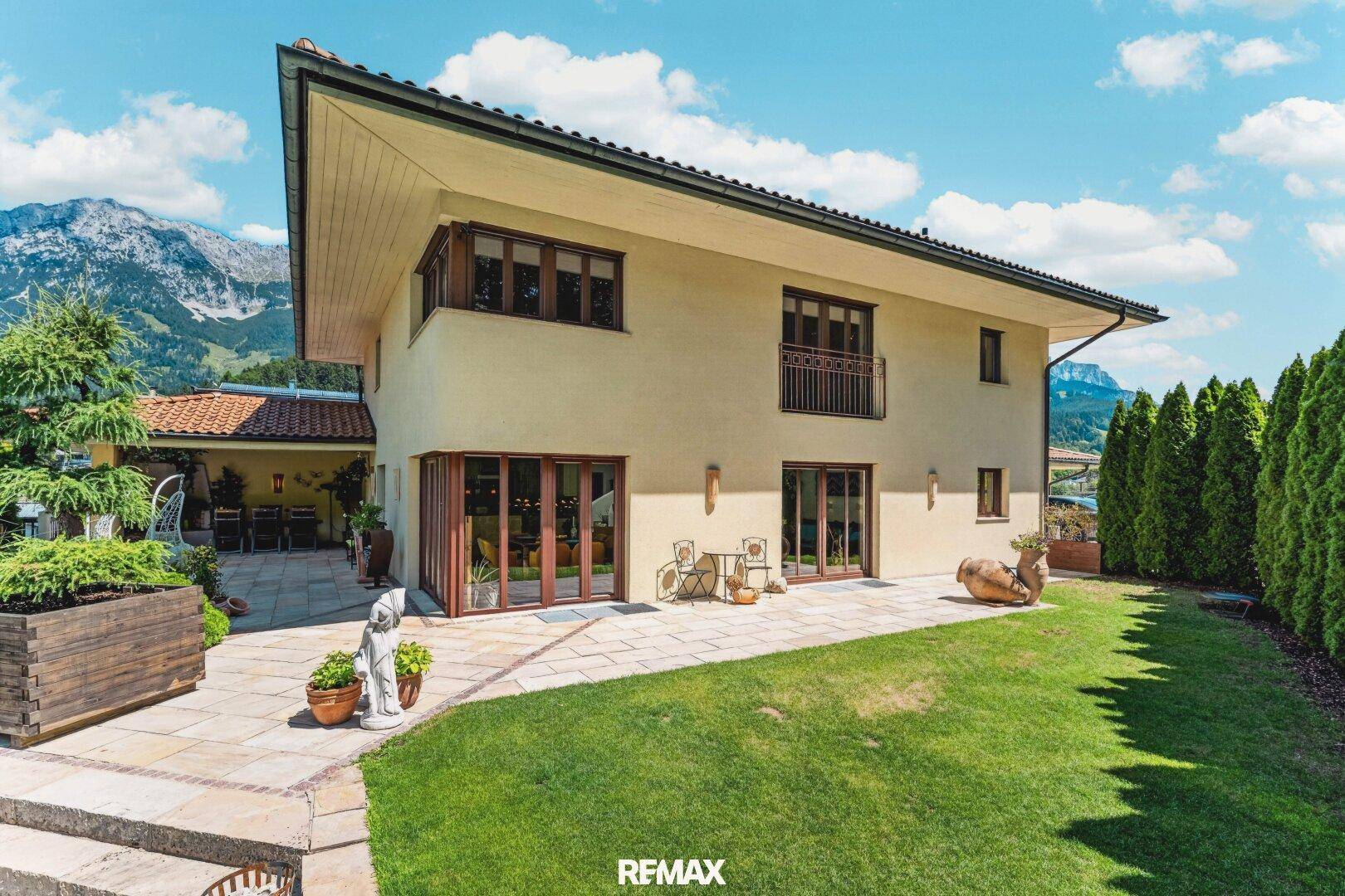 Rückansicht des Hauses mit Garten, Terrasse und Bergblick unter blauem Himmel.