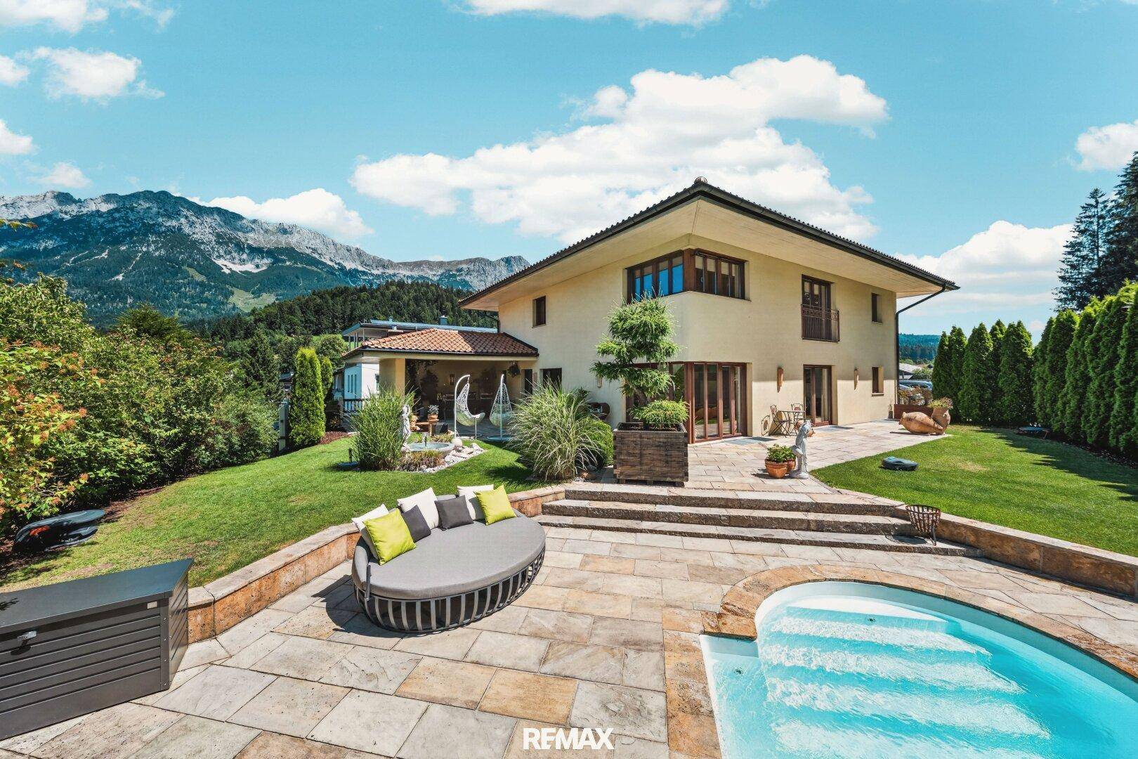 Großzügige Terrasse mit Pool und Liegebereich, umgeben von einem gepflegten Garten und Bergblick.