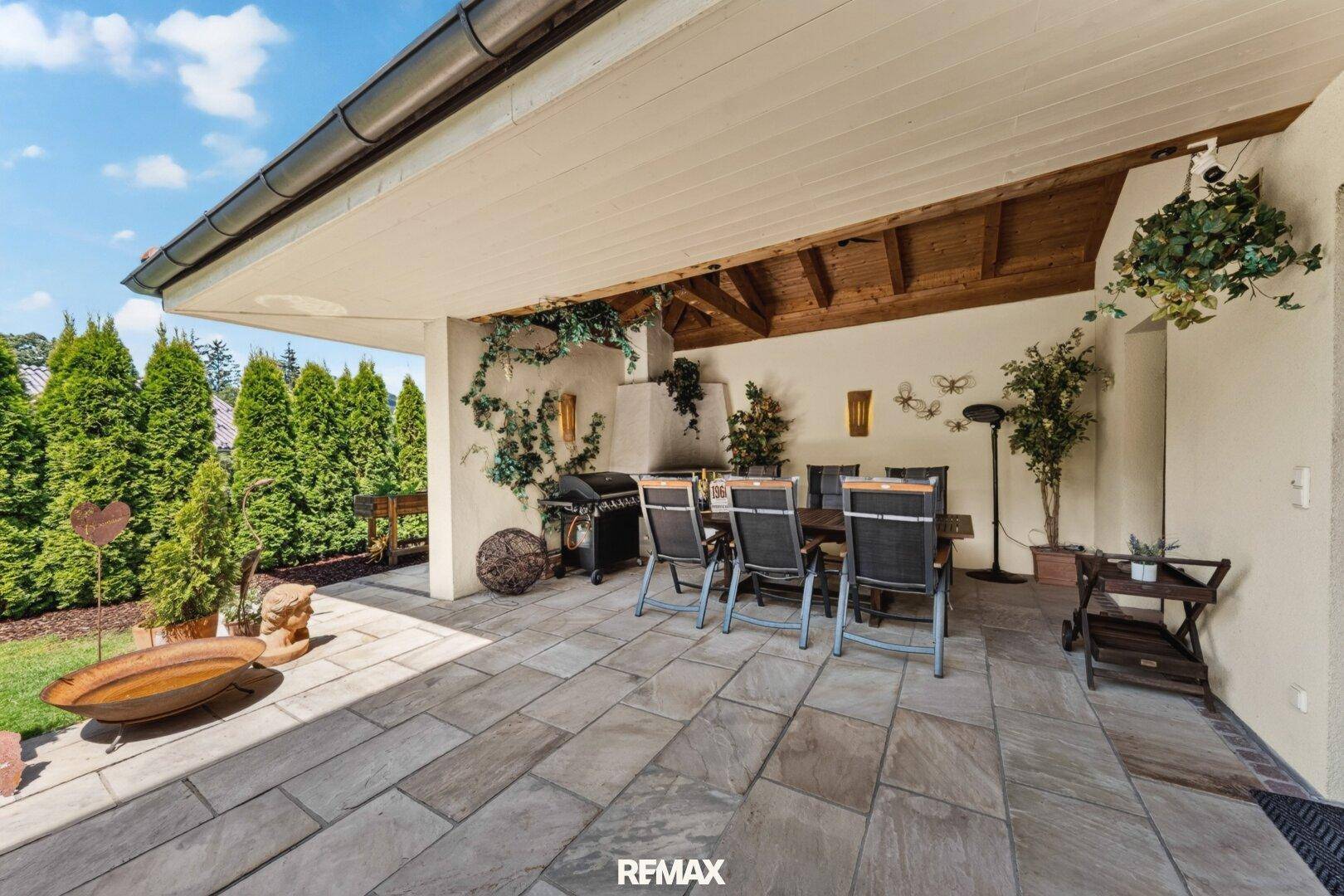 Überdachte Terrasse mit Grillbereich, Esstisch und Blick ins Grüne.