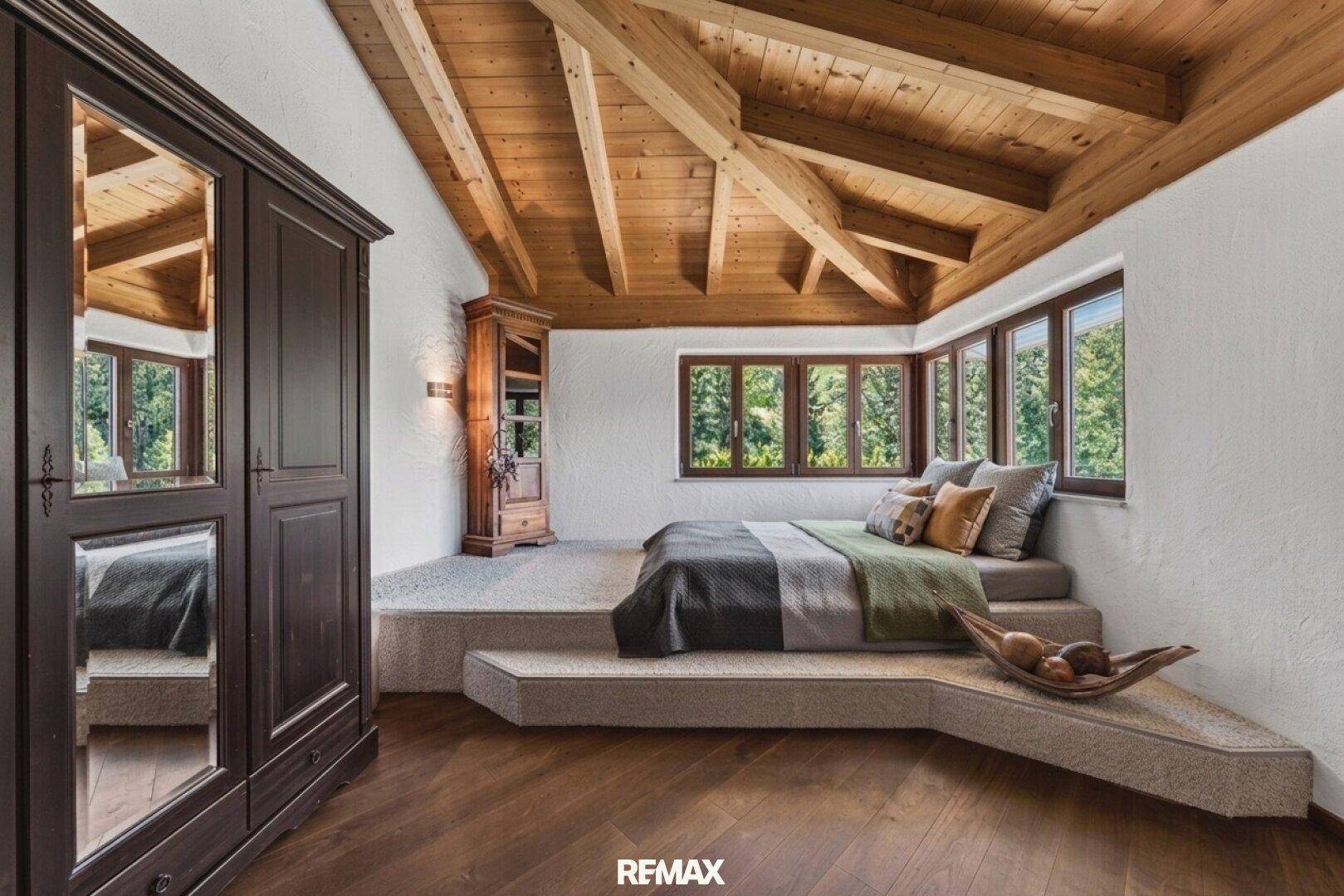 Schlafzimmer im Dachgeschoss mit Holzbalkendecke, erhöhtem Bettbereich und Holzboden.