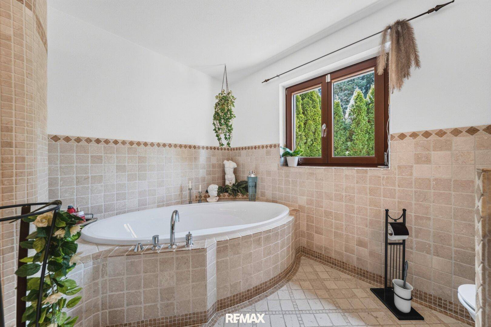 Geräumiges Badezimmer mit großer Badewanne, Fliesen und Fenster mit Blick ins Grüne.