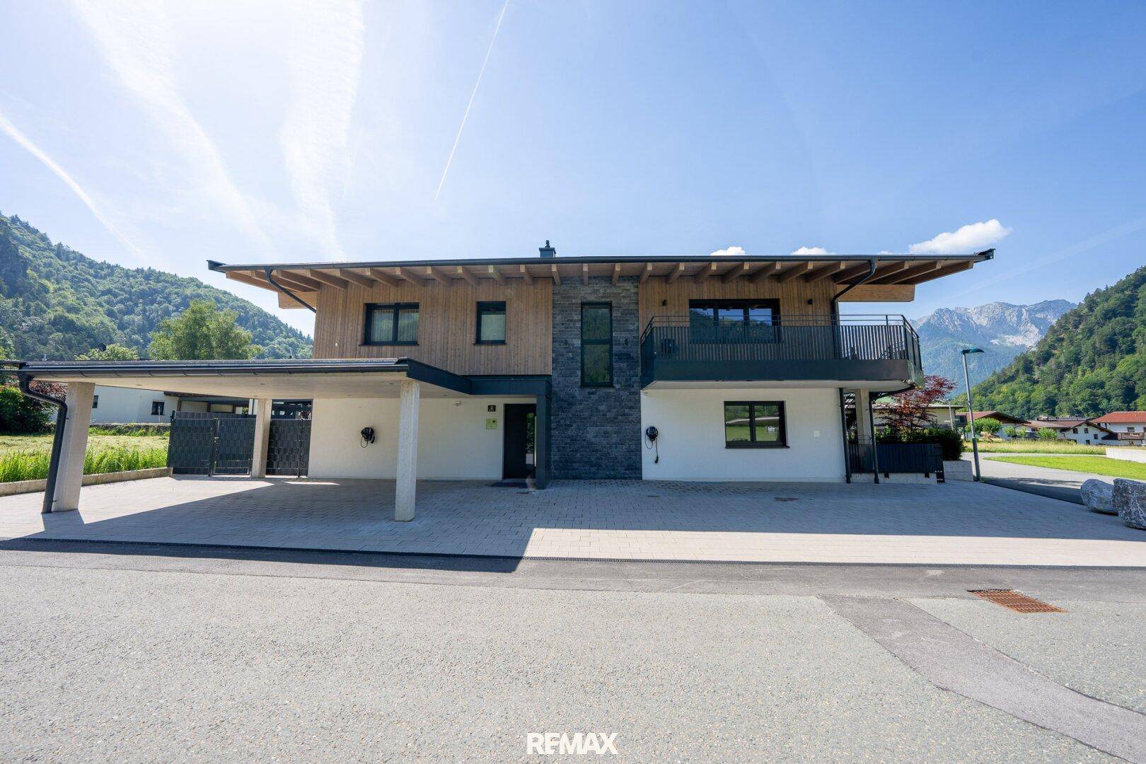 Weitläufige Ansicht der Hausfront mit Carport, Zufahrt und Bergpanorama im Hintergrund.