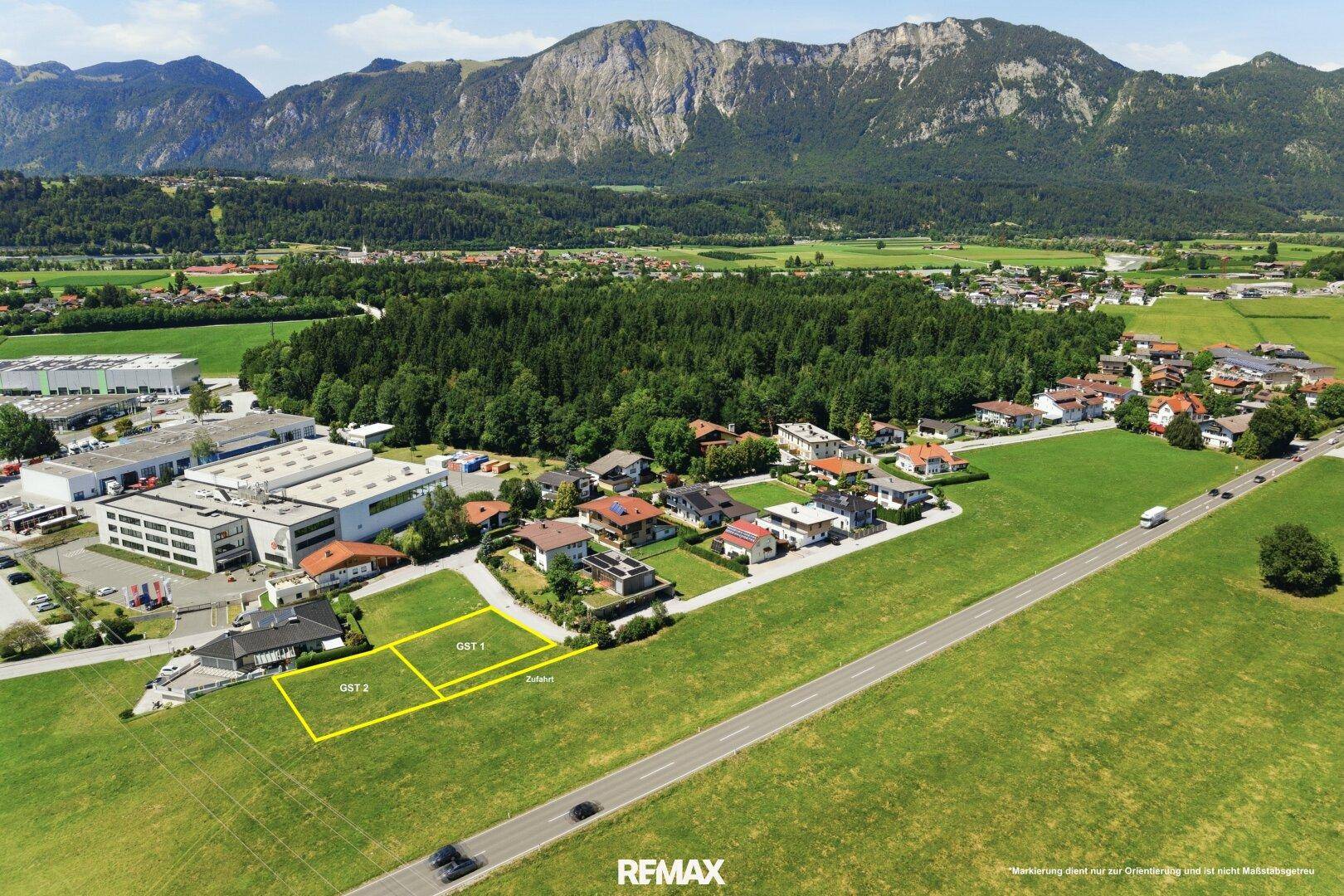 Luftaufnahme einer ländlichen Siedlung mit markierten Baugrundstücken und Bergpanorama.