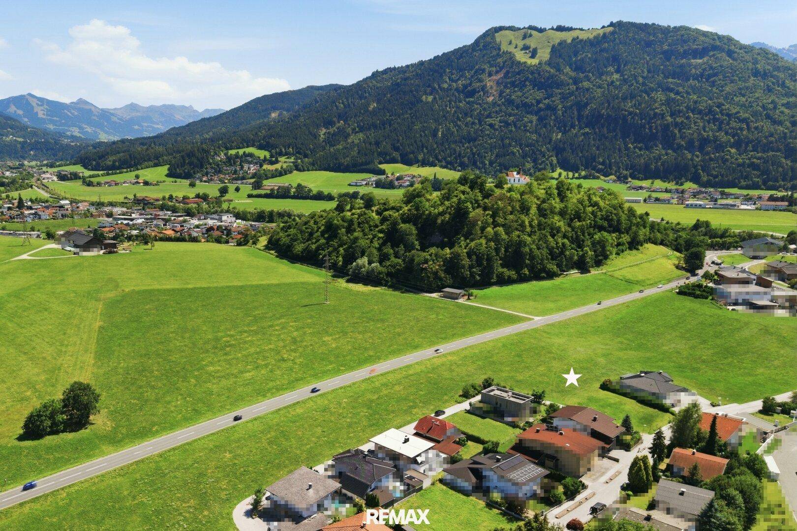 Luftaufnahme einer weiten grünen Landschaft mit Bergen und einem markierten Grundstück in der Ferne.