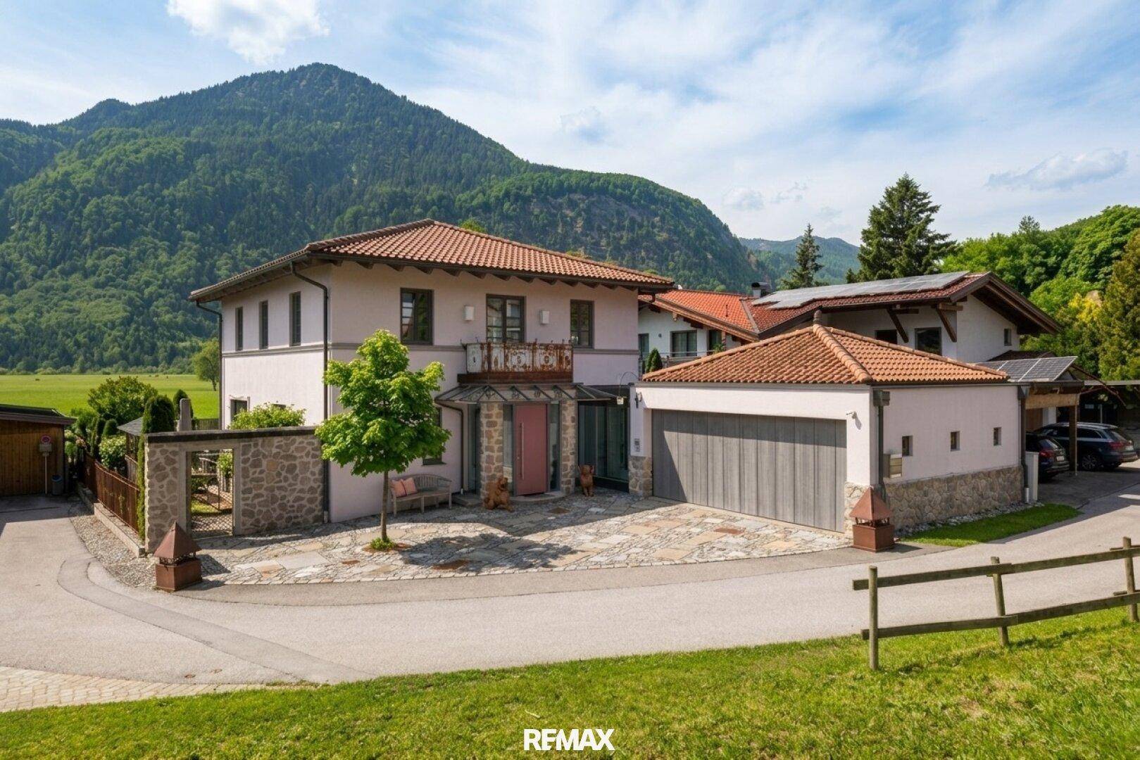 Attraktives Wohnhaus mit Doppelgarage und gepflegter Zufahrt in bergiger Landschaft.