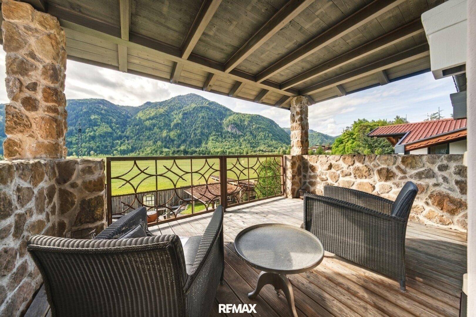 Überdachter Balkon mit Holzboden und Korbmöbeln, bietet einen weiten Blick auf die Berge.