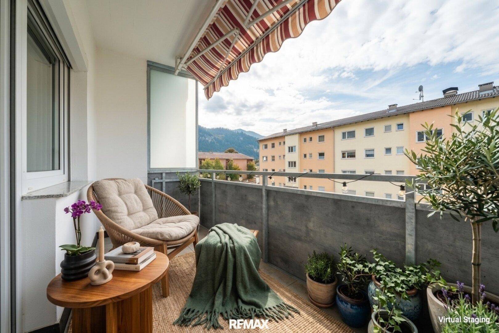 Möblierter Balkon mit Markise, Pflanzen und Blick auf die umliegenden Gebäude und Berge.