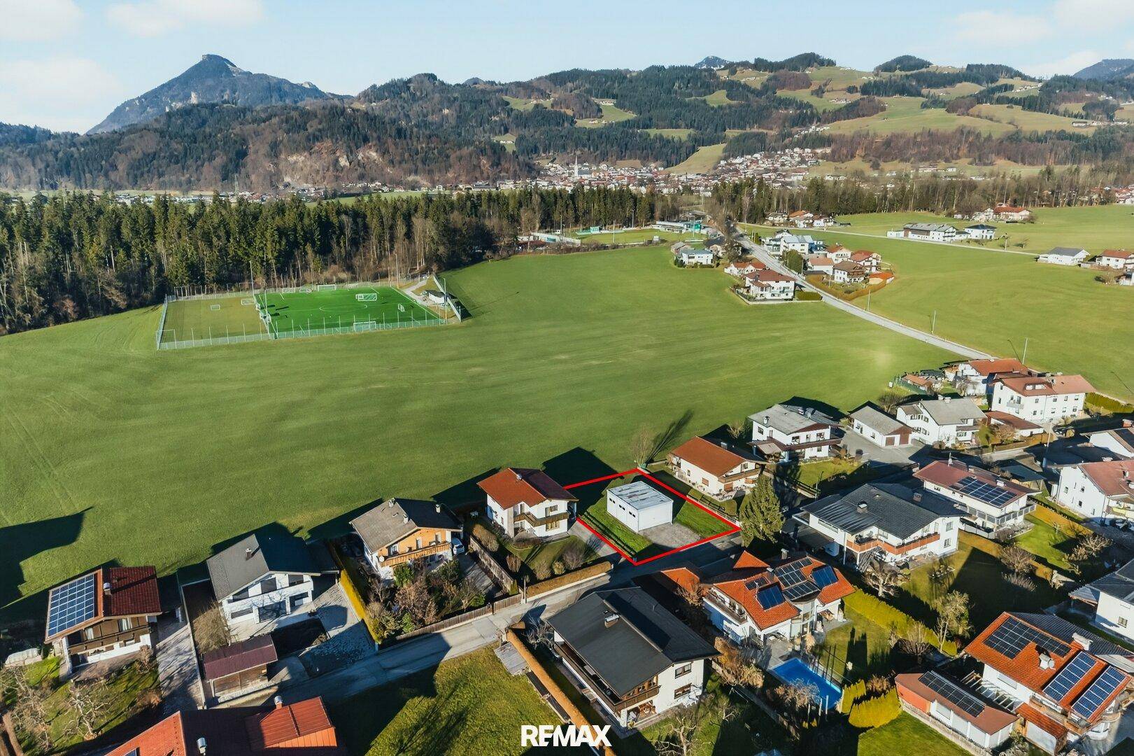Luftaufnahme des Grundstücks in einer ländlichen Umgebung mit angrenzenden Sportanlagen und Bergen.