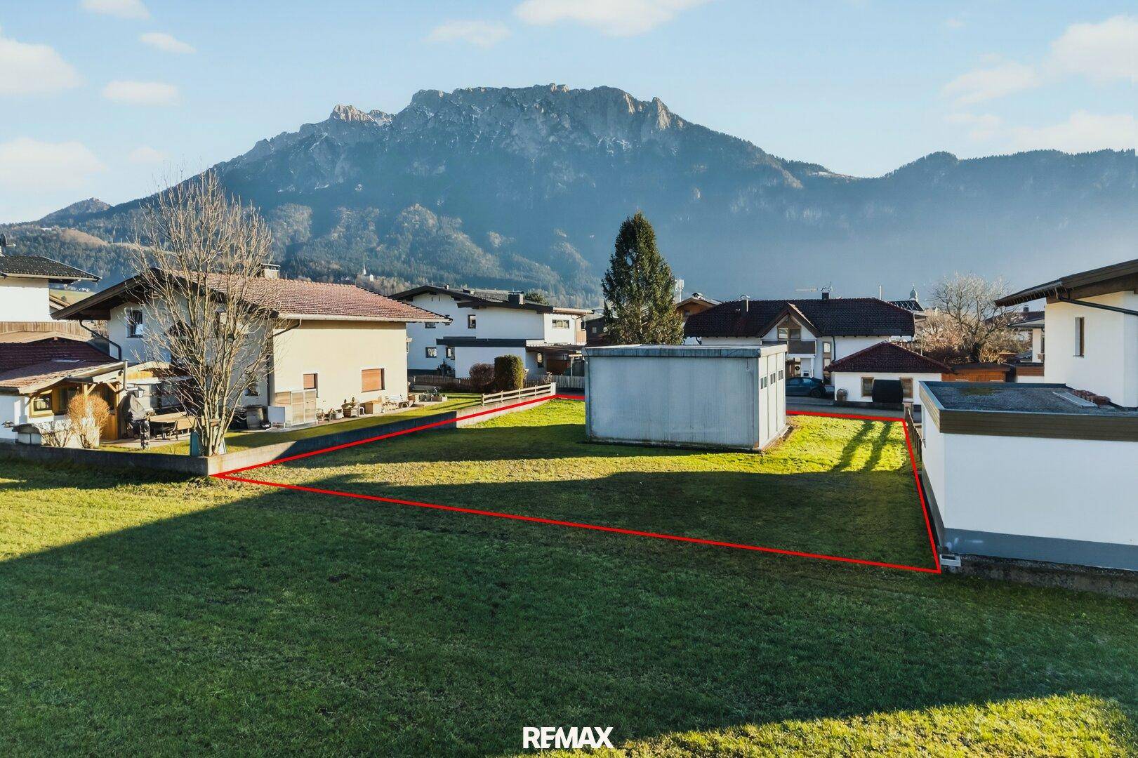 Blick vom Boden auf das grüne Grundstück mit einem Nebengebäude und der Bergkulisse im Hintergrund.