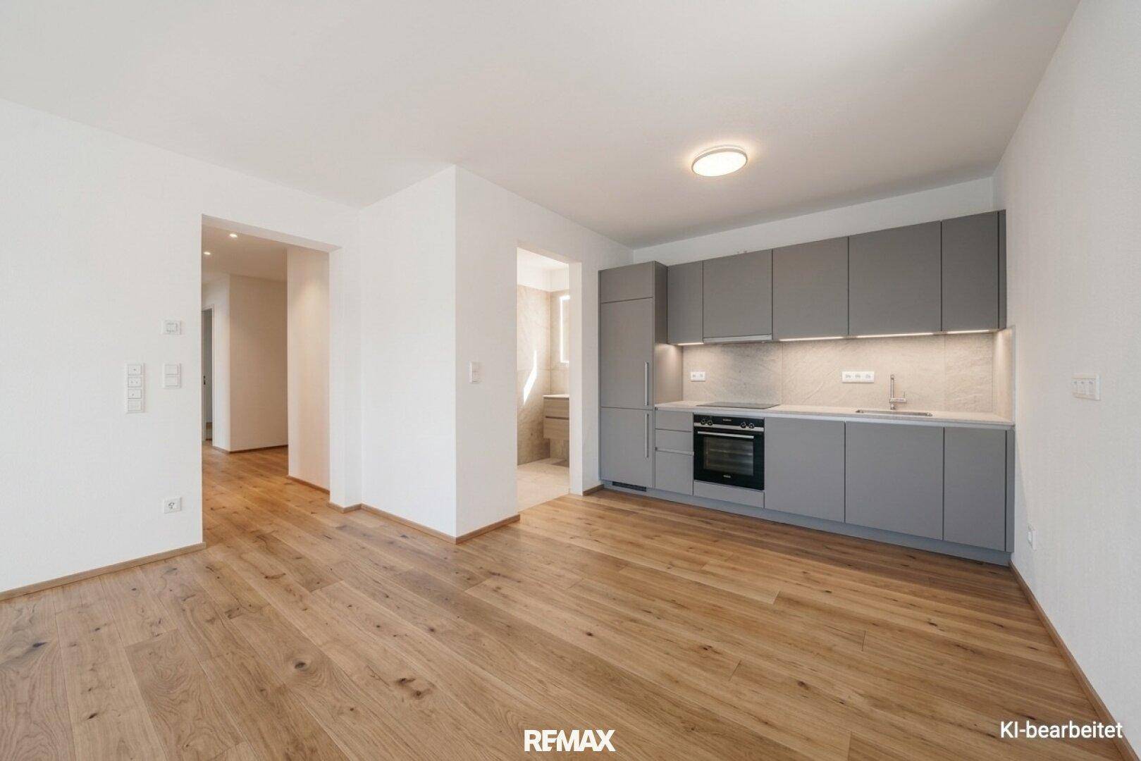 Moderne Einbauküche in Grau mit integrierten Geräten und Holzboden in einem offenen Wohnbereich.