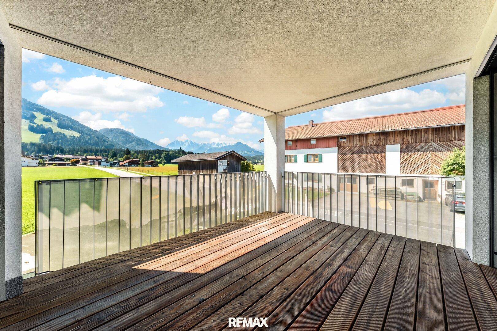 Geräumiger Balkon mit Holzbelag und Glasgeländer bietet einen weiten Blick auf die Berge und Natur.