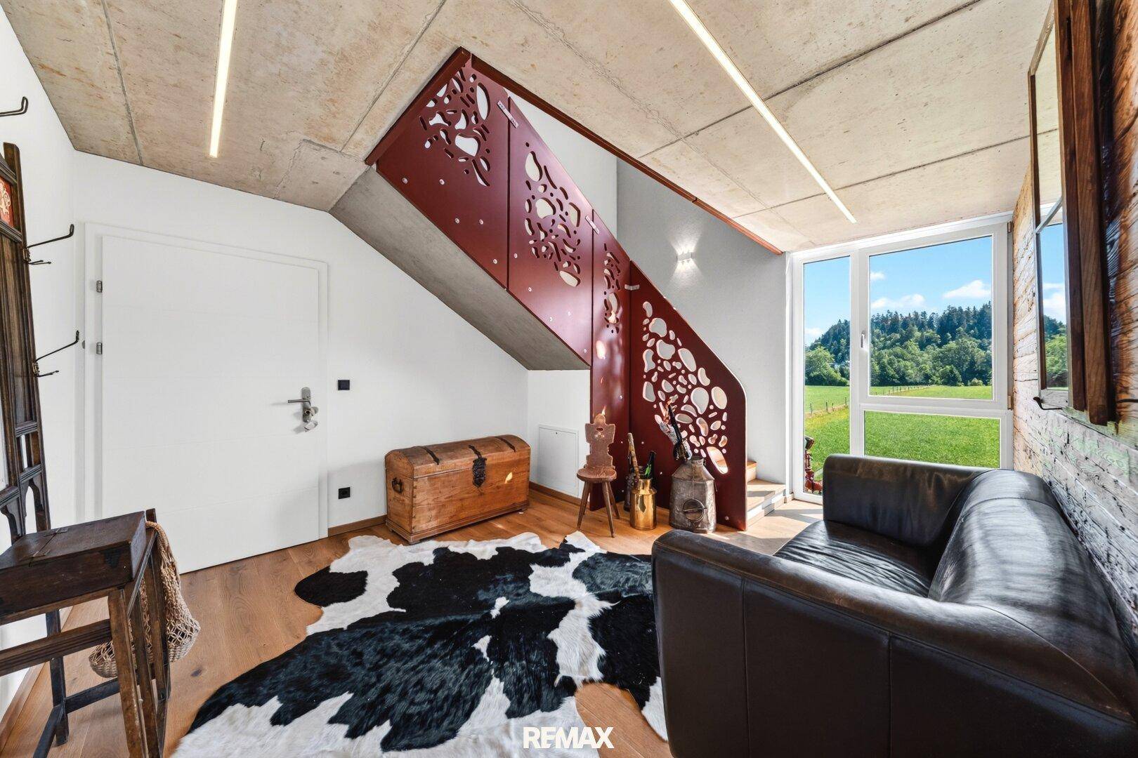 Eingangsbereich mit Holzboden, moderner Treppe und Blick ins Grüne durch große Fenster.
