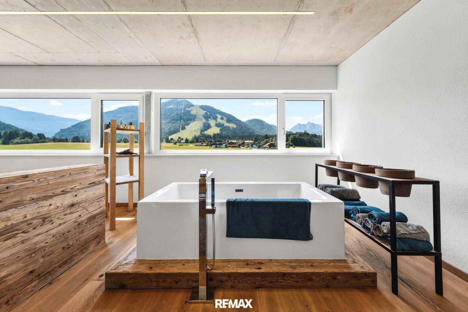 Modernes Badezimmer mit freistehender Badewanne, Holzboden und weitem Bergblick durch die Fenster.