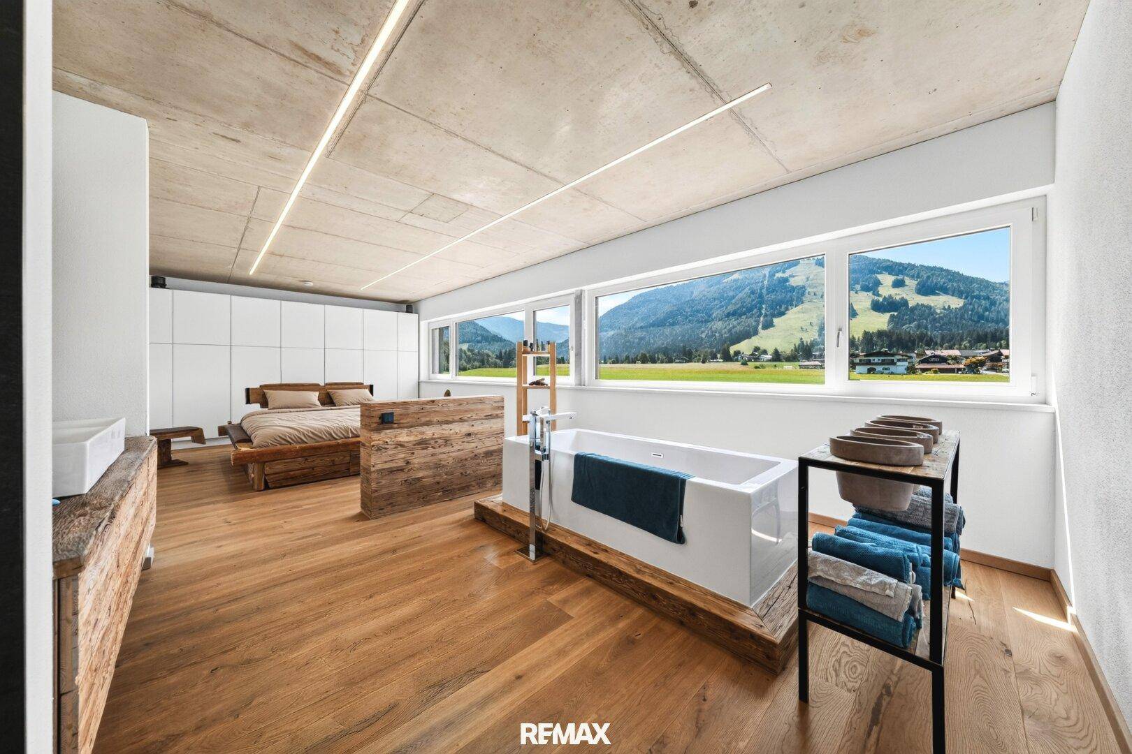 Offenes Schlafzimmer mit integrierter Badewanne, Holzboden und weitem Bergblick durch die Fenster.