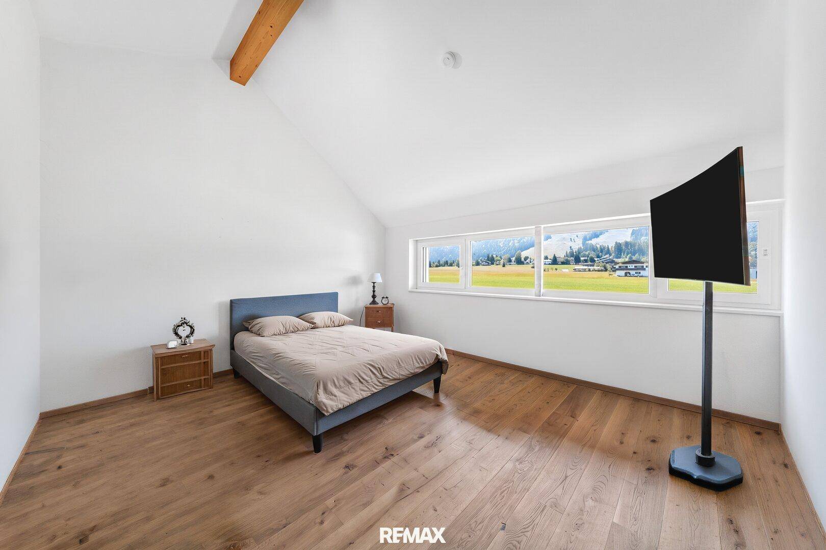Helles Schlafzimmer im Dachgeschoss mit Holzboden, sichtbaren Holzbalken und Bergblick.