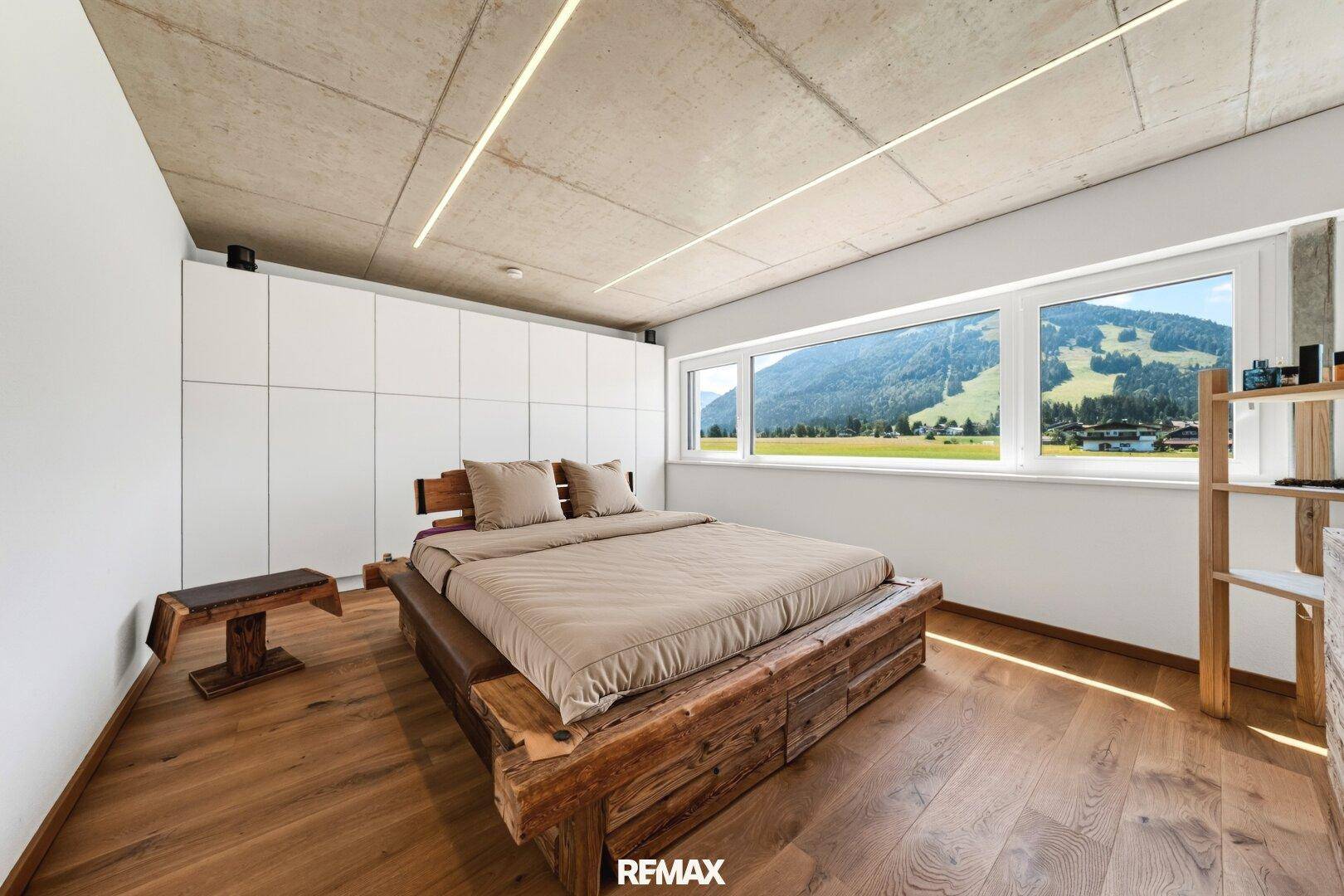 Schlafzimmer mit rustikalem Holzbett, Einbauschränken und Panoramafenstern mit Bergblick.