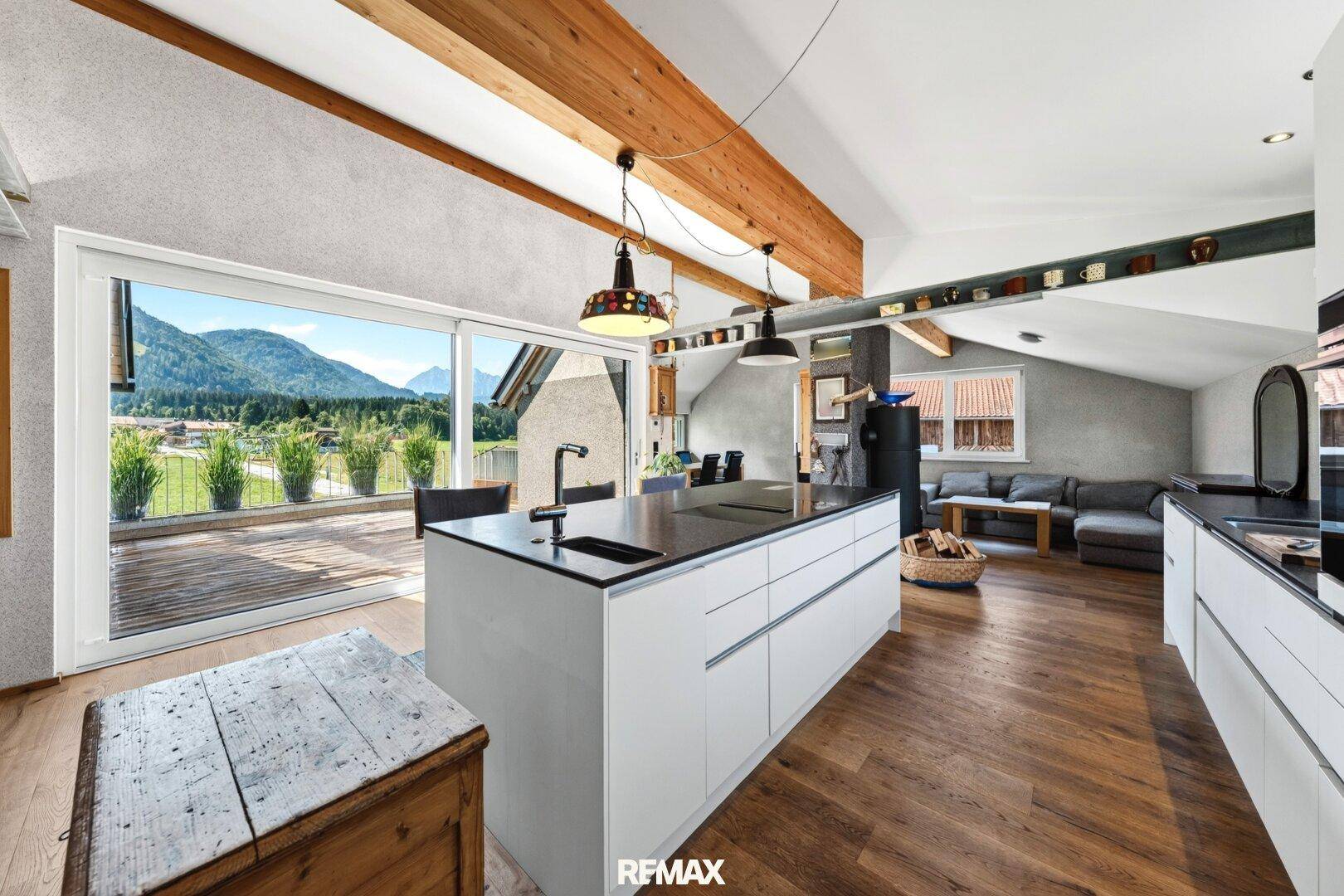 Heller offener Wohnbereich mit moderner Küche, Kücheninsel, Holzboden und Zugang zur Terrasse.