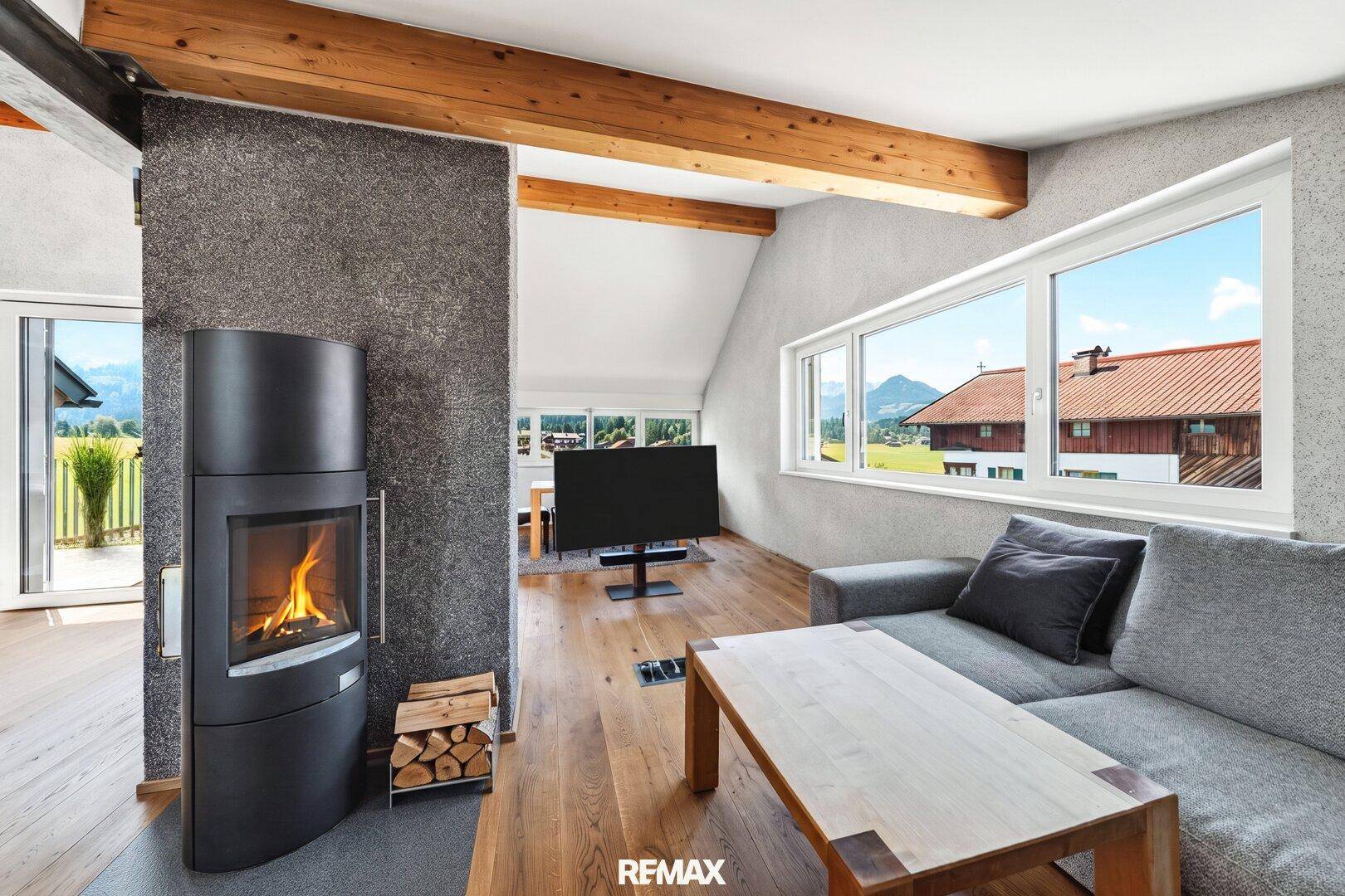 Gemütliches Wohnzimmer mit modernem Kaminofen, Holzboden, Holzbalken und Bergblick.