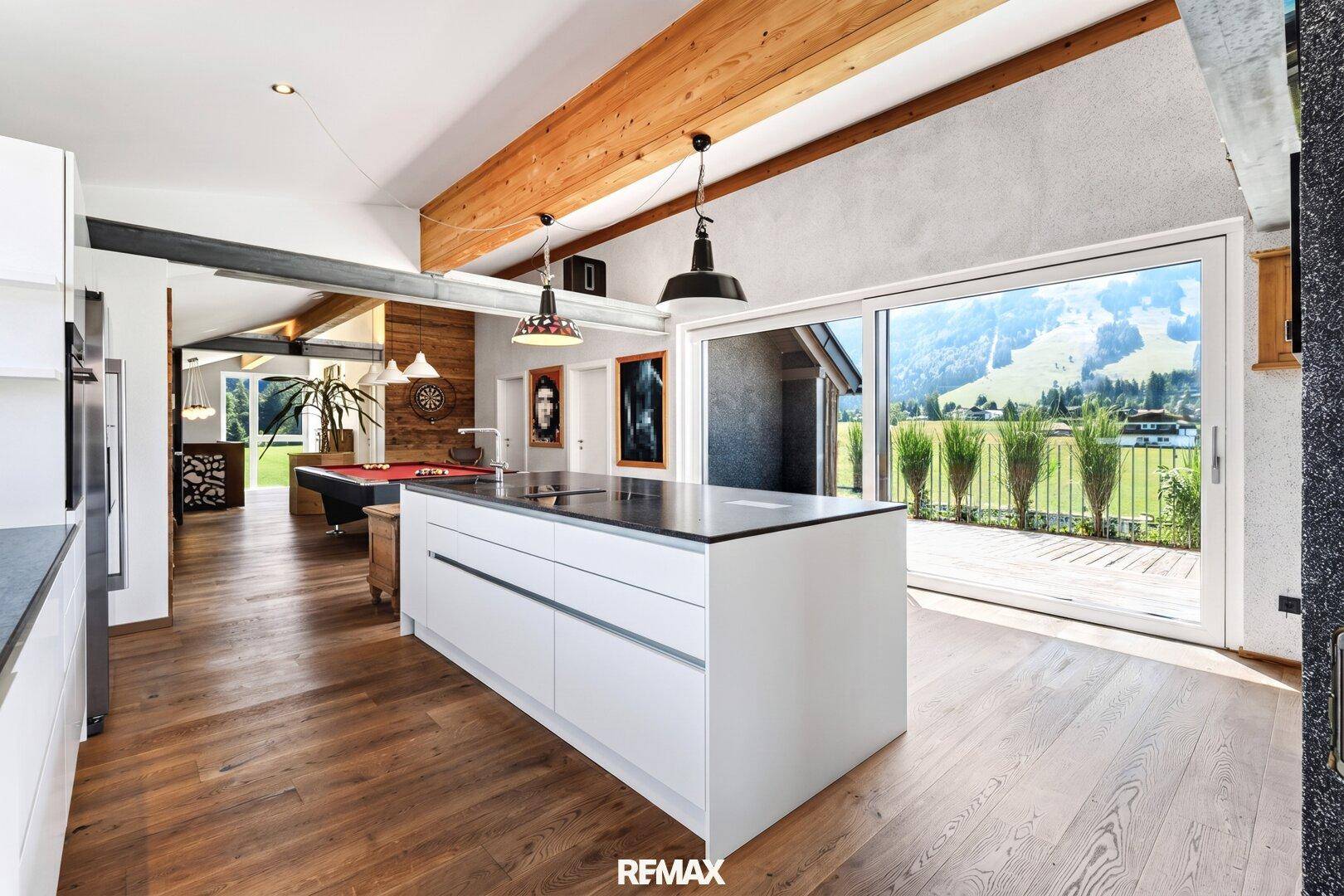 Geräumiger offener Wohnbereich mit Küche, Billardtisch, Holzboden und Terrassenzugang mit Bergblick.