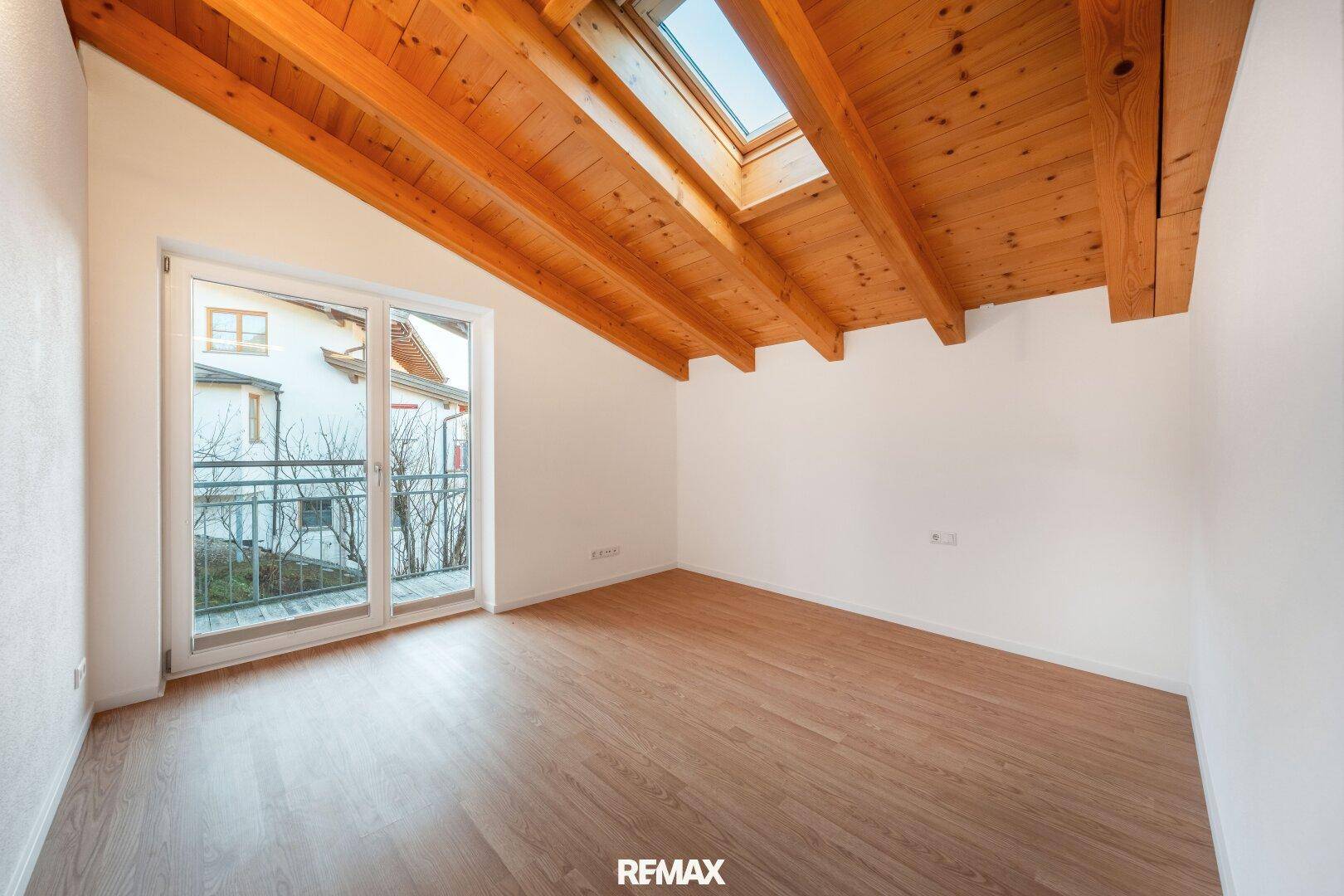 Helles Zimmer im Dachgeschoss mit Holzbalkendecke, Dachfenster und Balkonzugang.