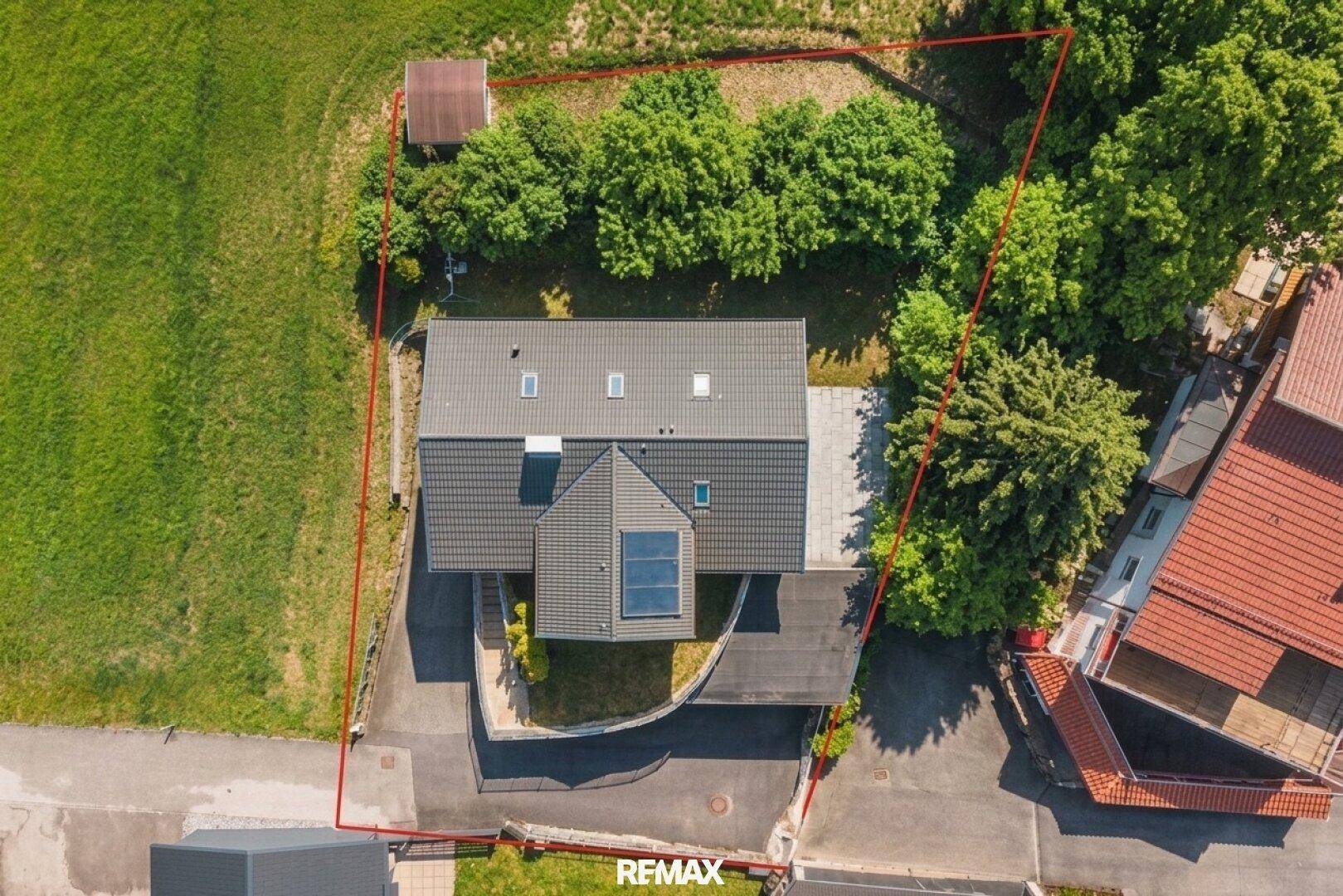 Draufsicht des Hauses mit Dachfenstern, Grundstücksgrenzen und umliegenden Bäumen.