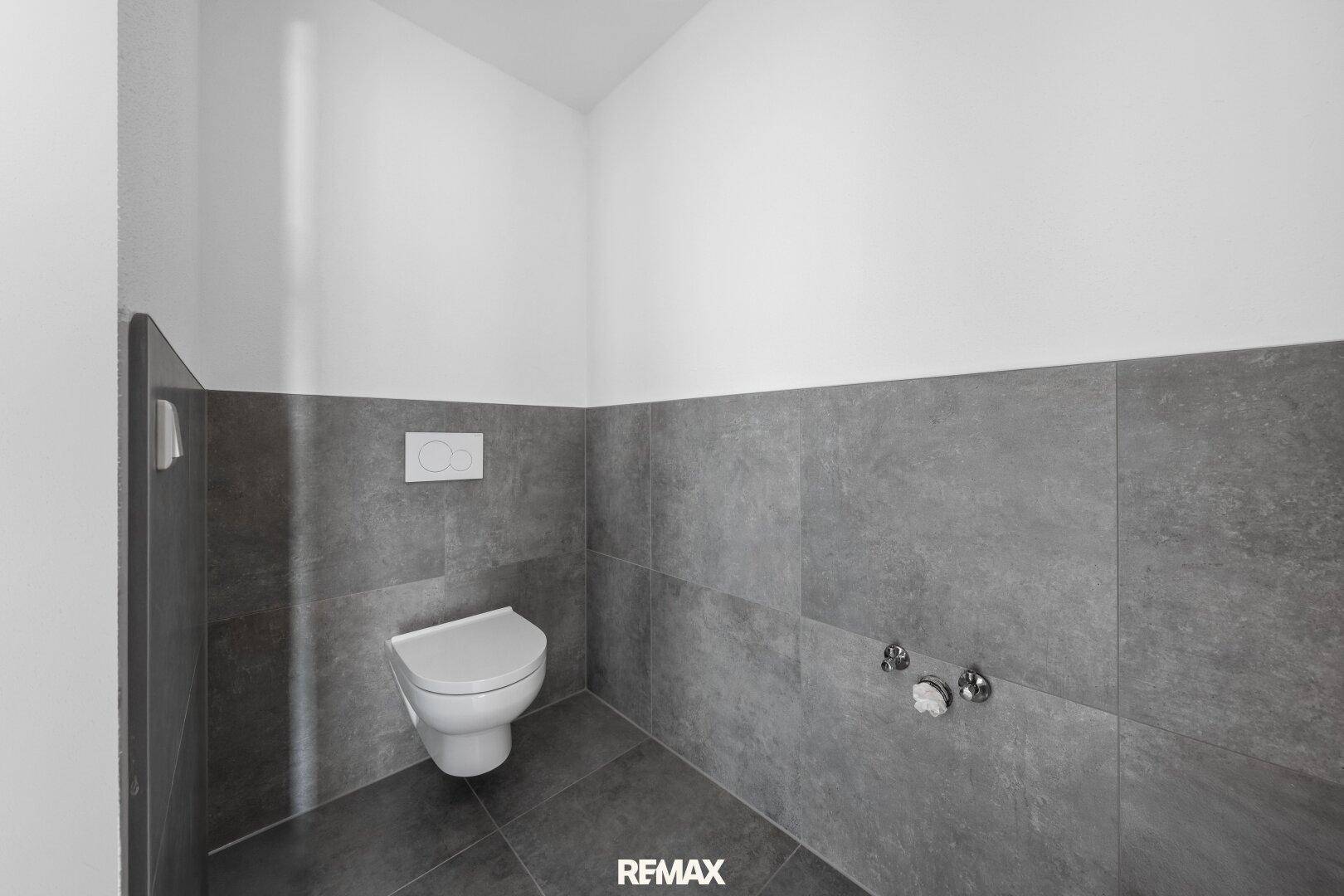 Modernes Gäste-WC mit grauen Fliesen und wandhängendem WC, noch im Ausbau.