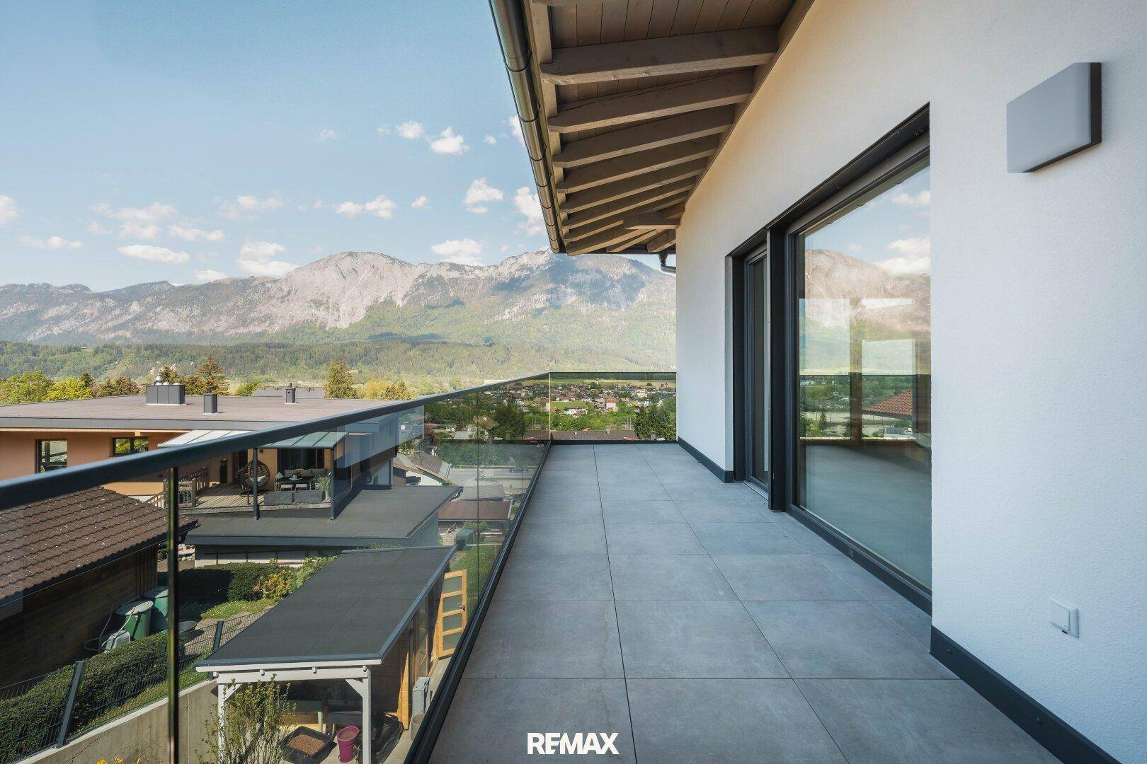 Langer Balkon mit Glasgeländer und Fliesenboden, bietet einen weiten Blick auf die Berge.