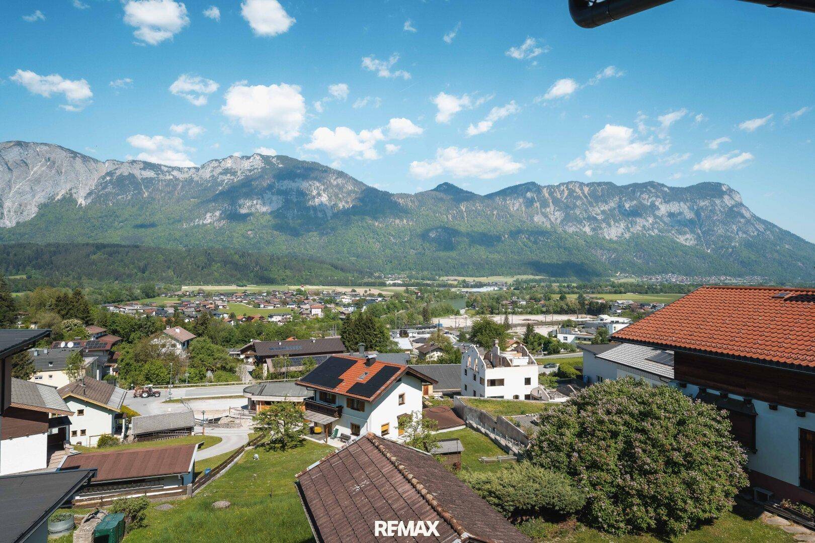 Panoramablick über ein grünes Tal mit Bergen und umliegenden Wohnhäusern.