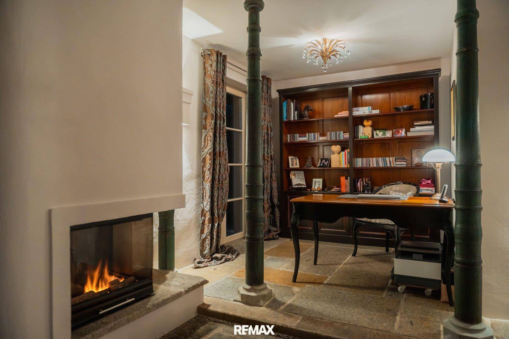 Arbeitszimmer mit Kamin, Steinfußboden und einem großen Bücherregal, das zum Verweilen einlädt.