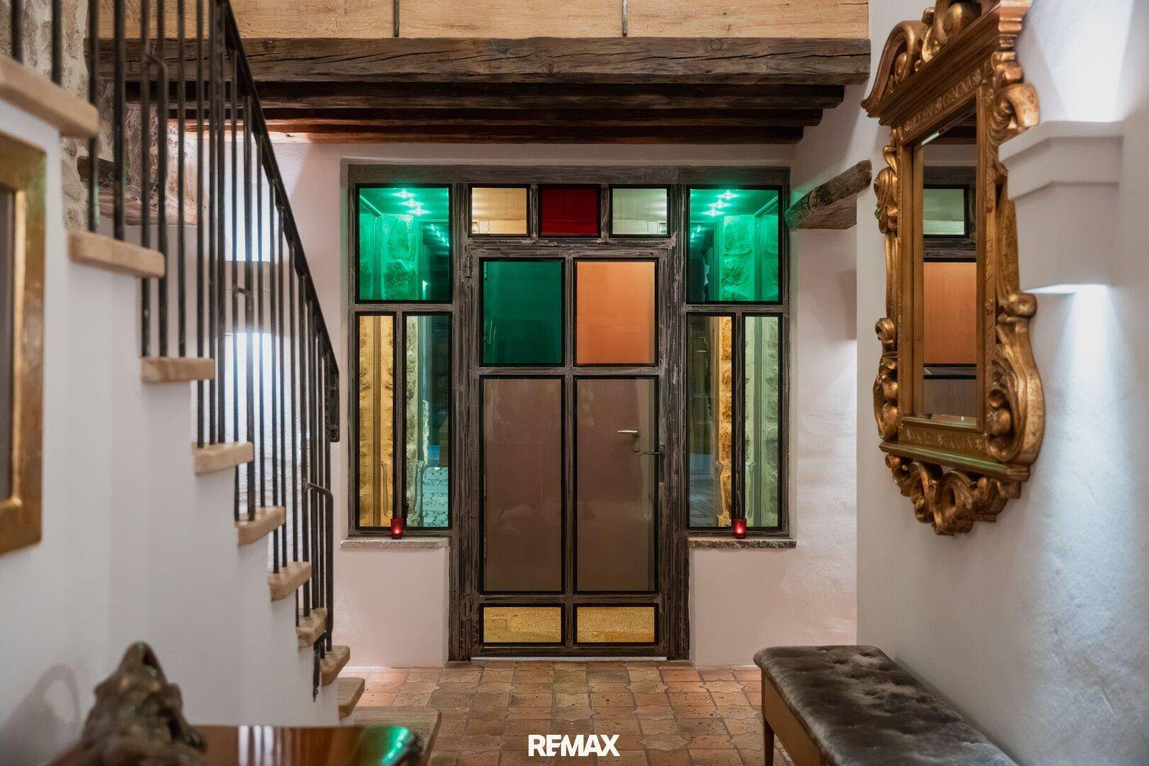 Einladender Eingangsbereich mit farbigen Glasfenstern, Holzbalken und einer eleganten Treppe.
