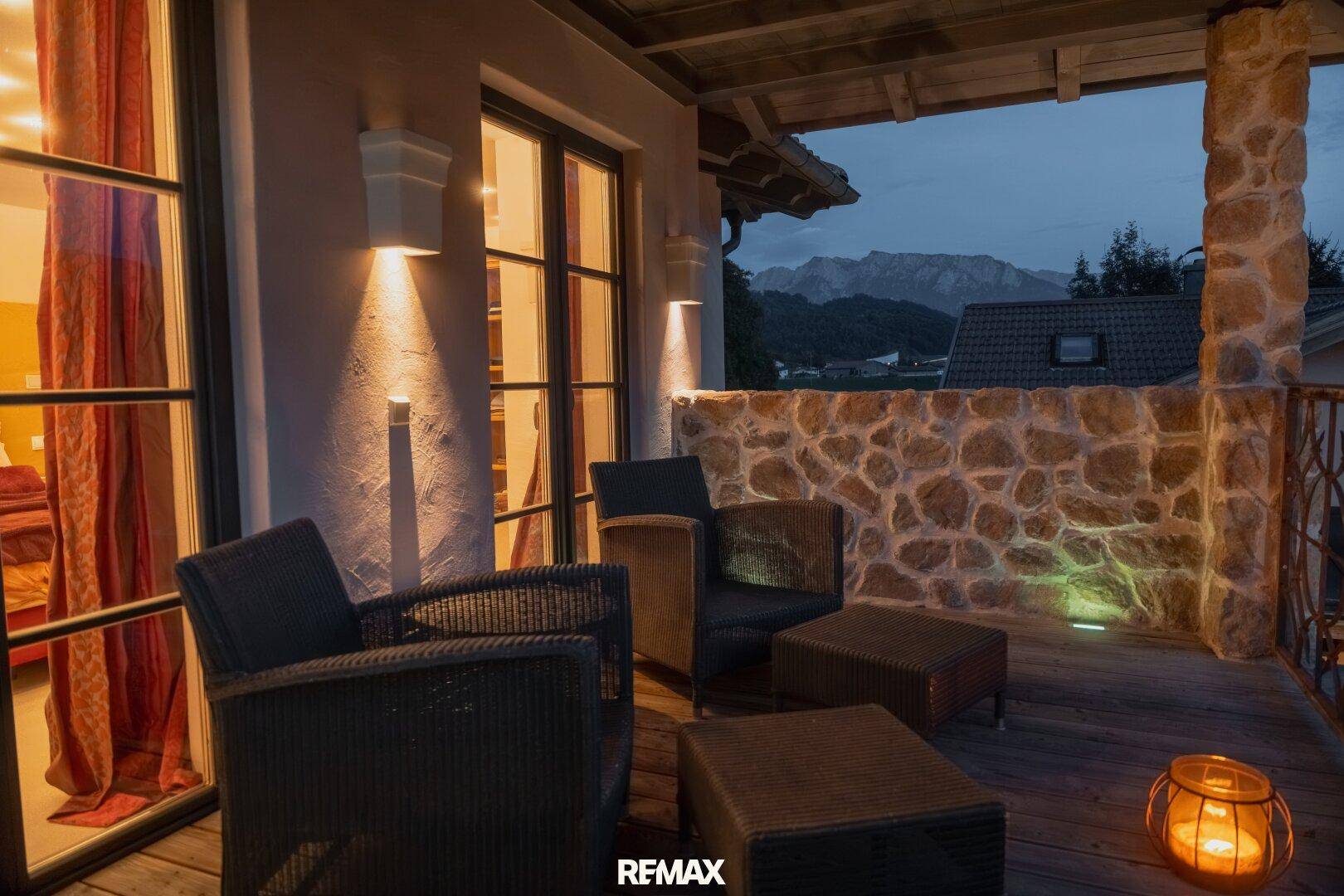 Gemütlicher Balkon mit Korbmöbeln, Steinmauer und Blick auf die umliegende Berglandschaft.