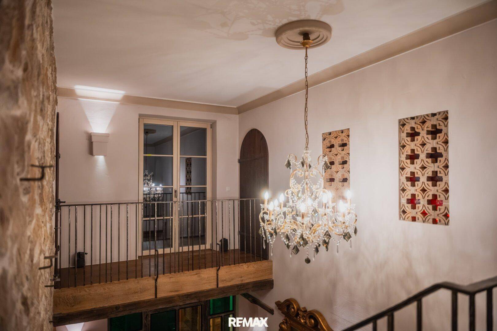 Heller Treppenabsatz mit Kronleuchter, Steinwand und Zugang zu weiteren Räumen.