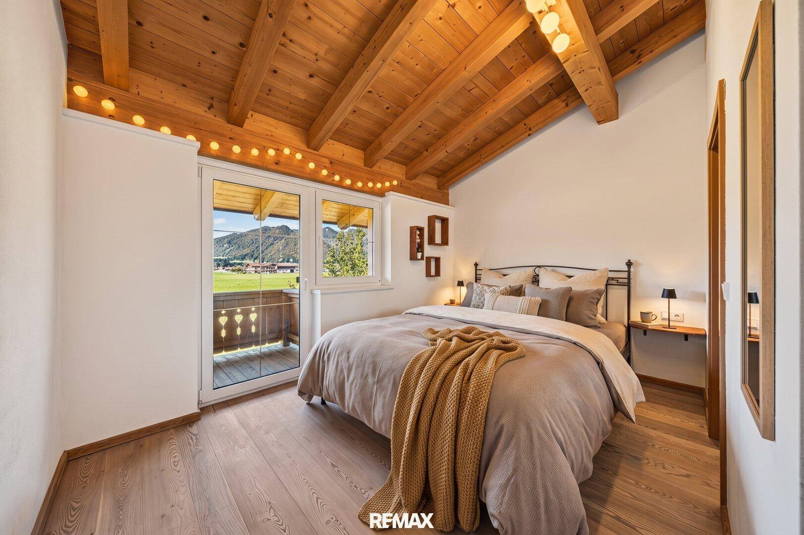 Helles Schlafzimmer mit Holzbalkendecke, Holzboden und Zugang zum Balkon.