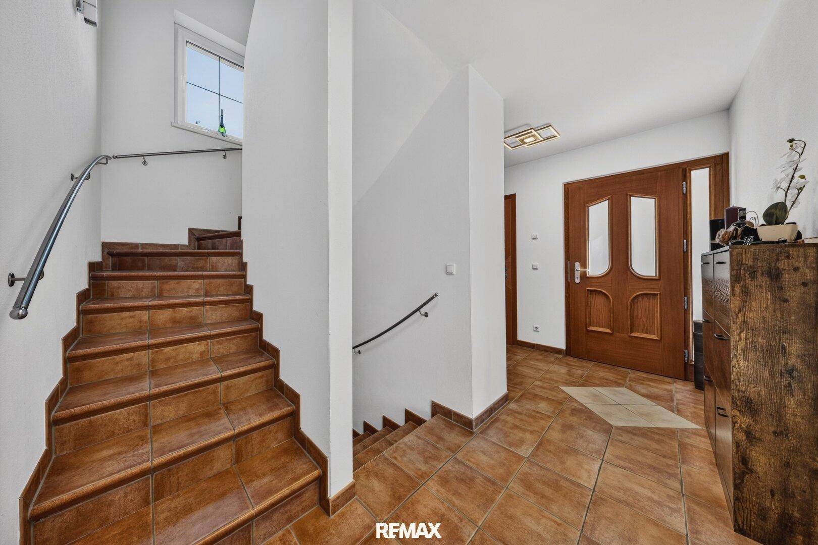Heller Eingangsbereich mit Holztreppe und Fliesenboden, der zu den oberen Etagen führt.