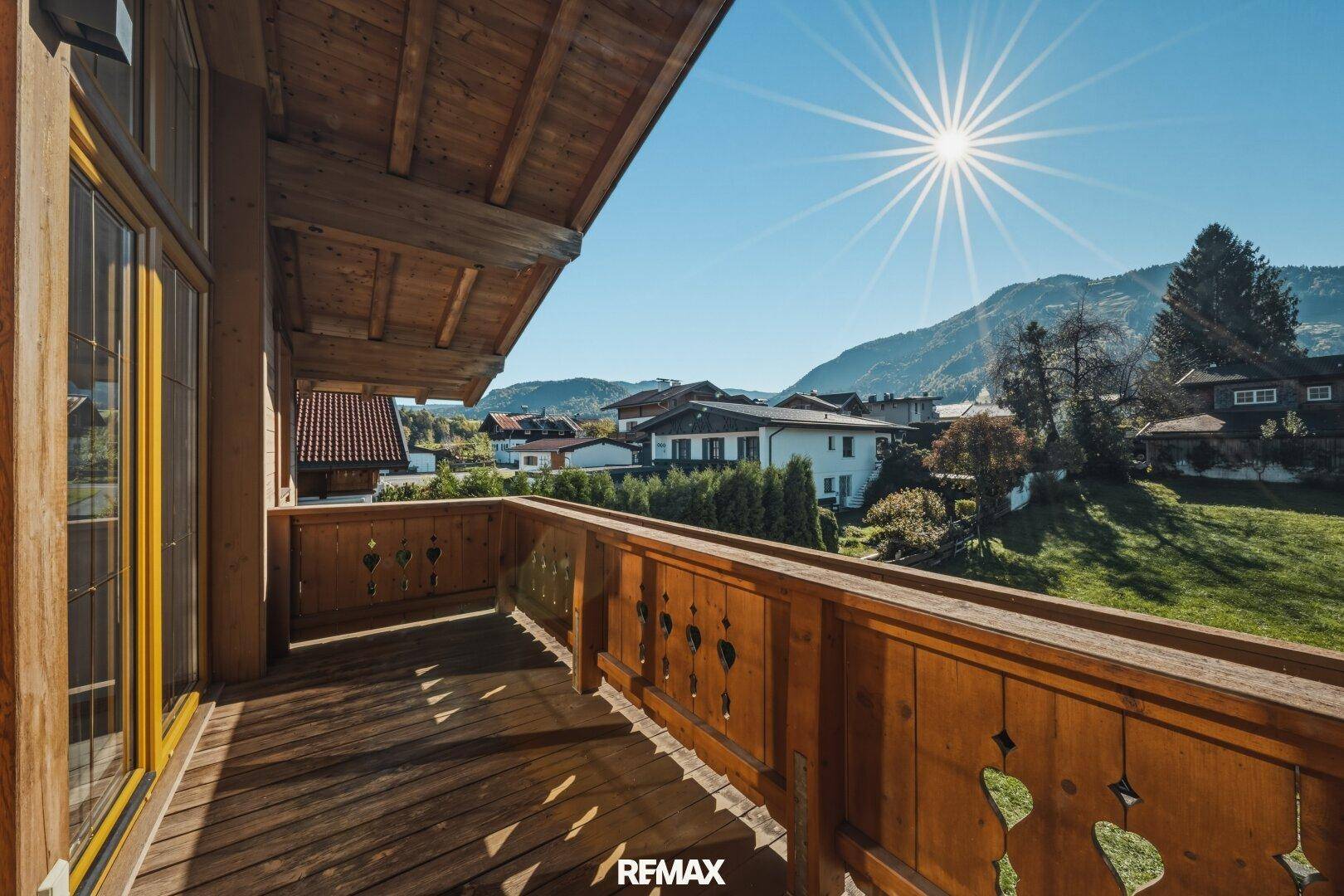 Sonniger Holzbalkon mit traditionellem Geländer und weitem Blick auf die Berglandschaft.
