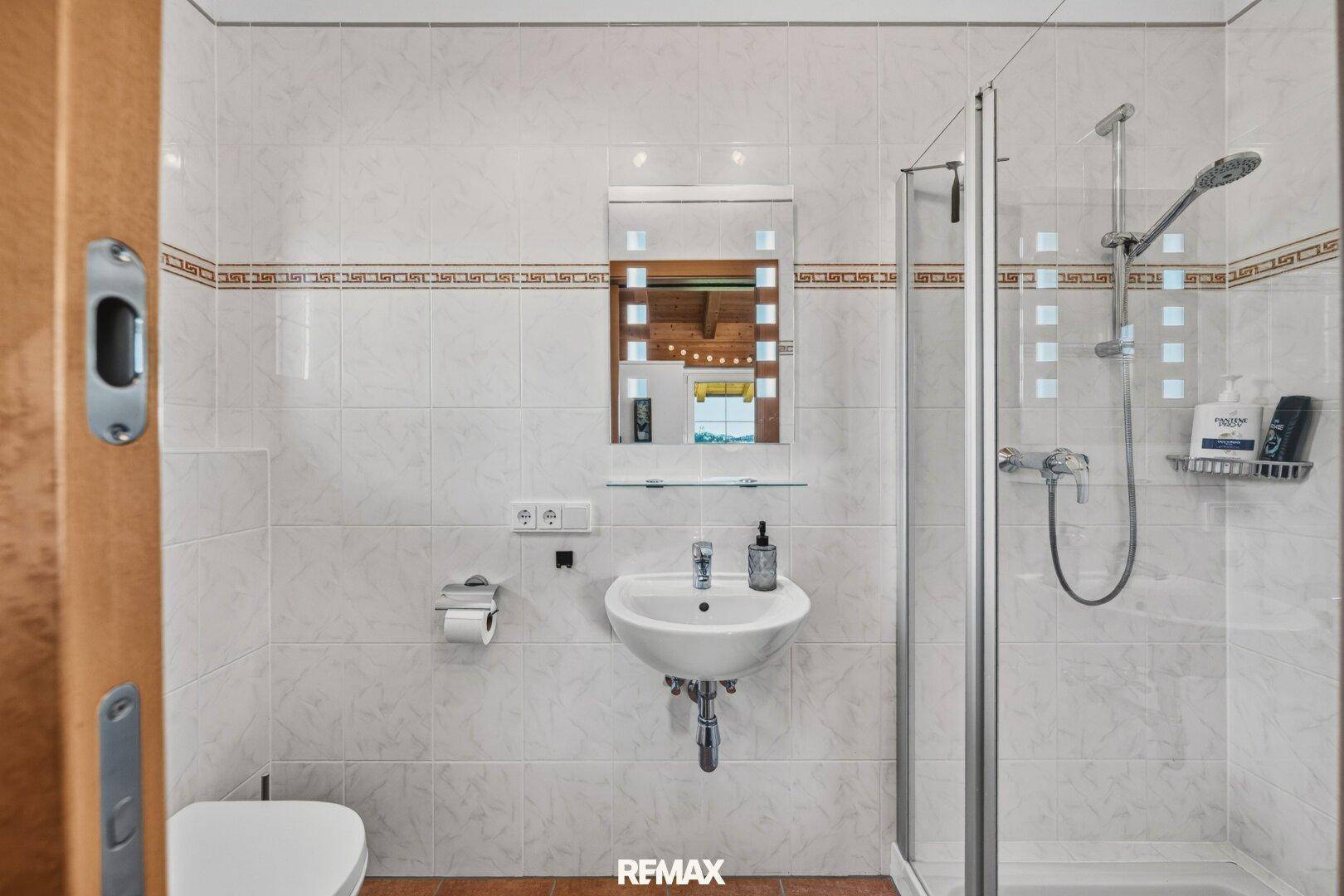 Funktionales Badezimmer mit Dusche, Waschbecken und hellen Fliesen.