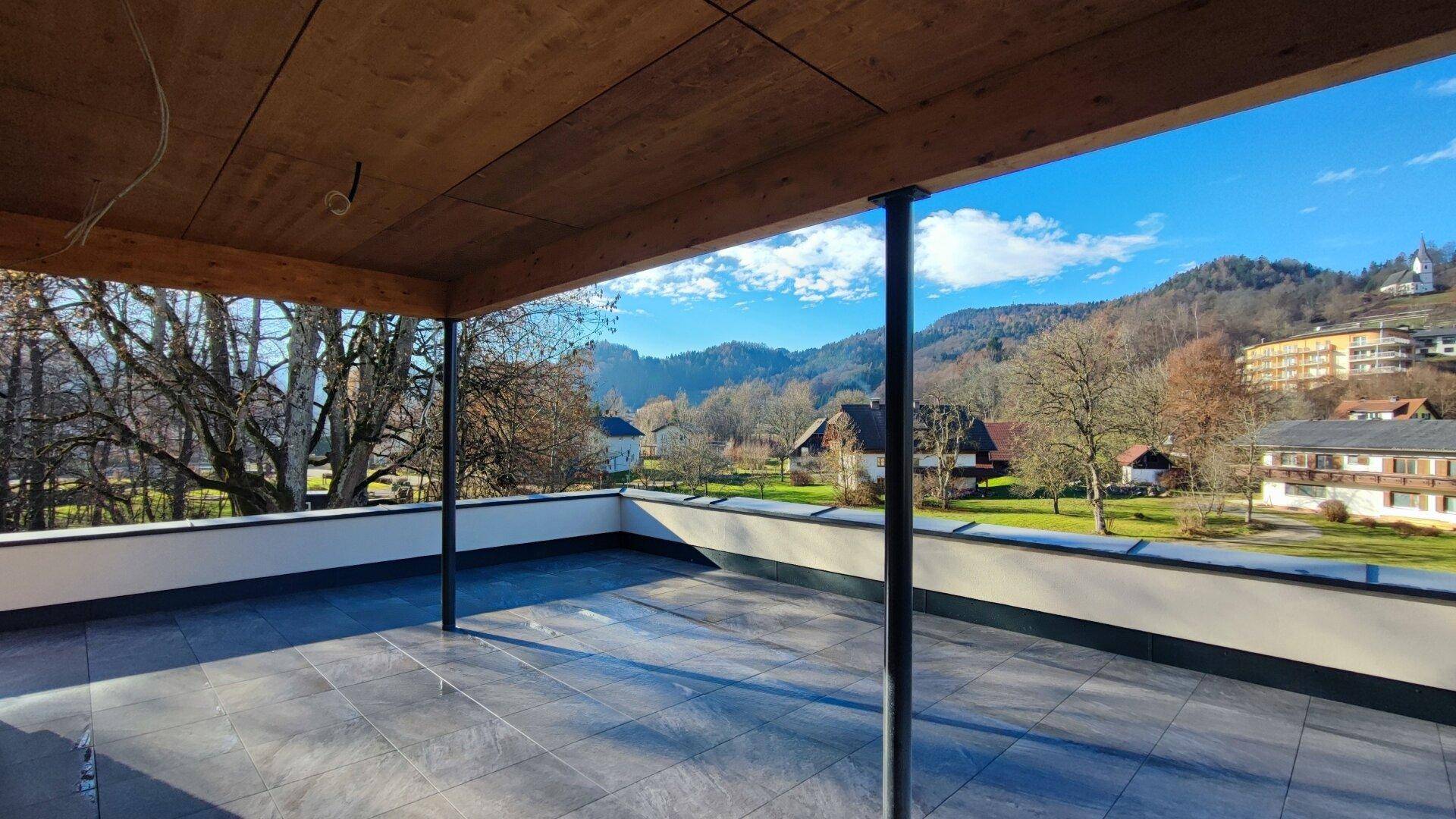 Große überdachte Terrasse mit Fliesenboden und weitem Blick auf die grüne Umgebung.